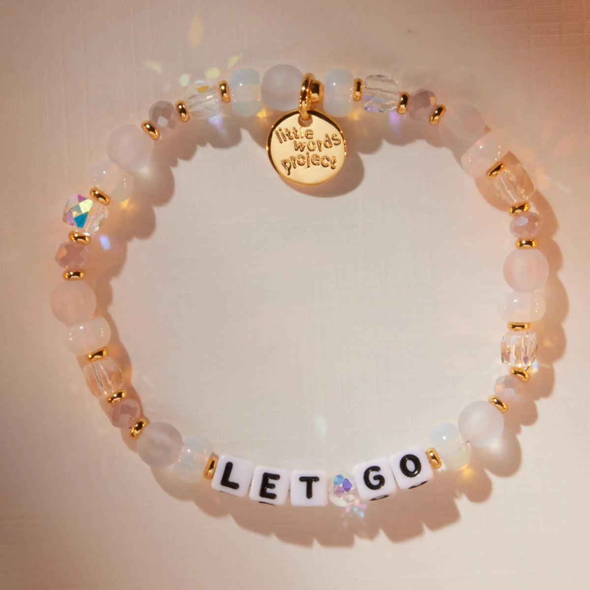 Let Go bracelet in the Marshmellow bead pattern with white letter beads, flat-lay on warm neutral background with soft light