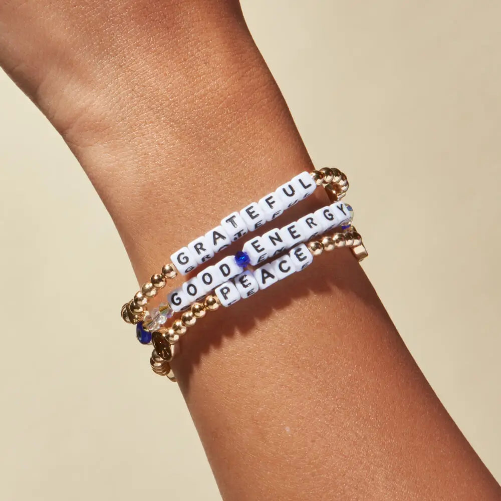 Bracelets with motivational phrases on a wrist against a beige background
