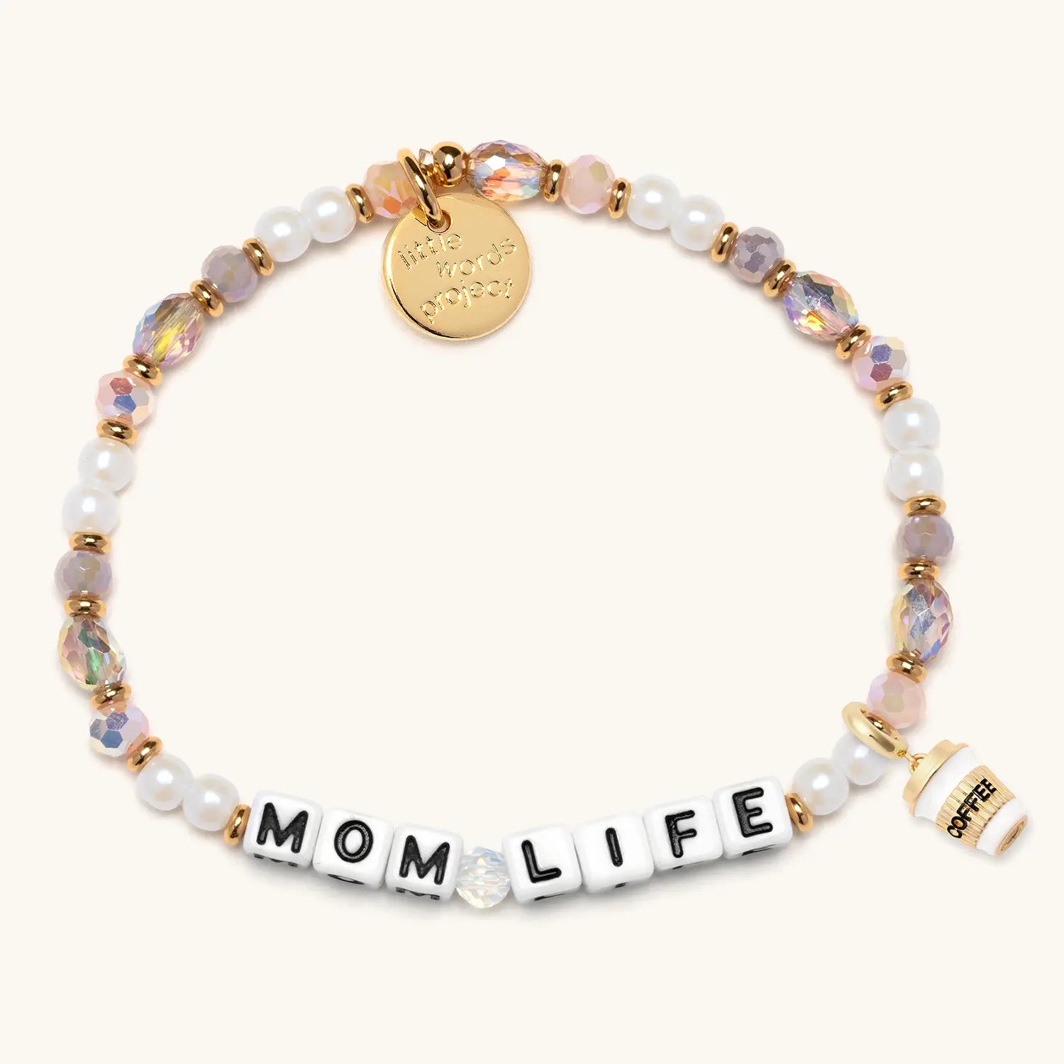 A stretch beaded bracelet featuring a mix of white pearl beads, iridescent pink and lavender faceted crystal beads, and small gold spacer beads. White square letter beads spell out "MOM LIFE" in black lettering. A circular gold embossed charm hangs from the top, and a small gold-trimmed white enamel coffee cup charm hangs from the side. Photographed on a white background.