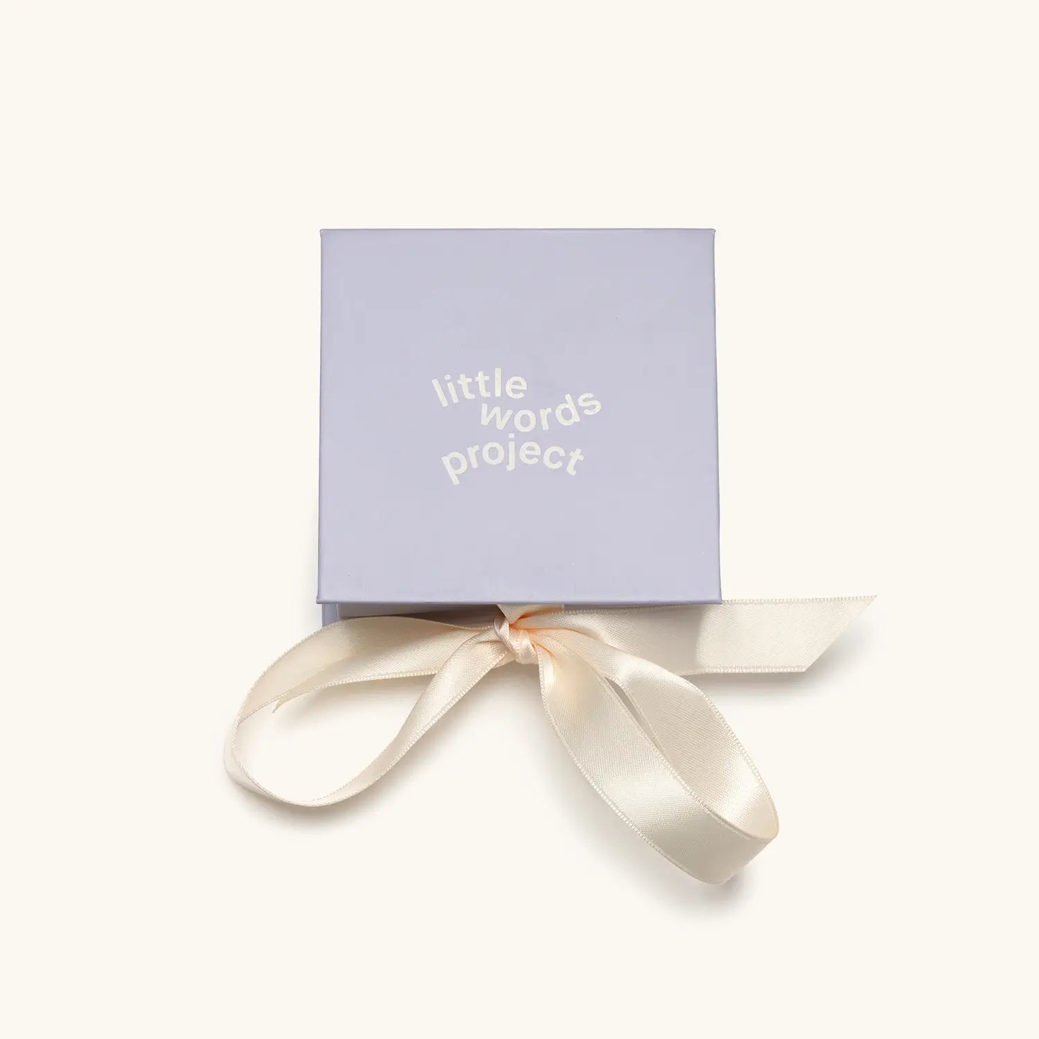 A small square lavender gift box with "little words project" printed in white text on the lid, tied with a cream satin ribbon bow.