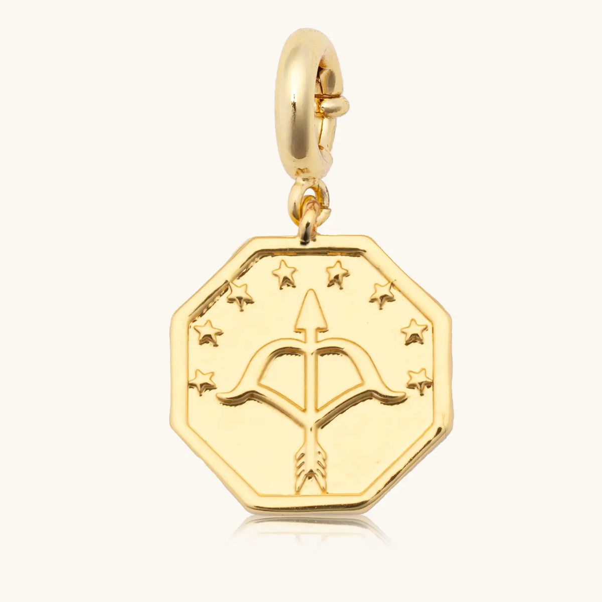 Keep Moving Forward Charm back, 18k gold-plated octagon medallion with a bow and arrow framed in stars on a gold spring ring clasp, detail on cream background