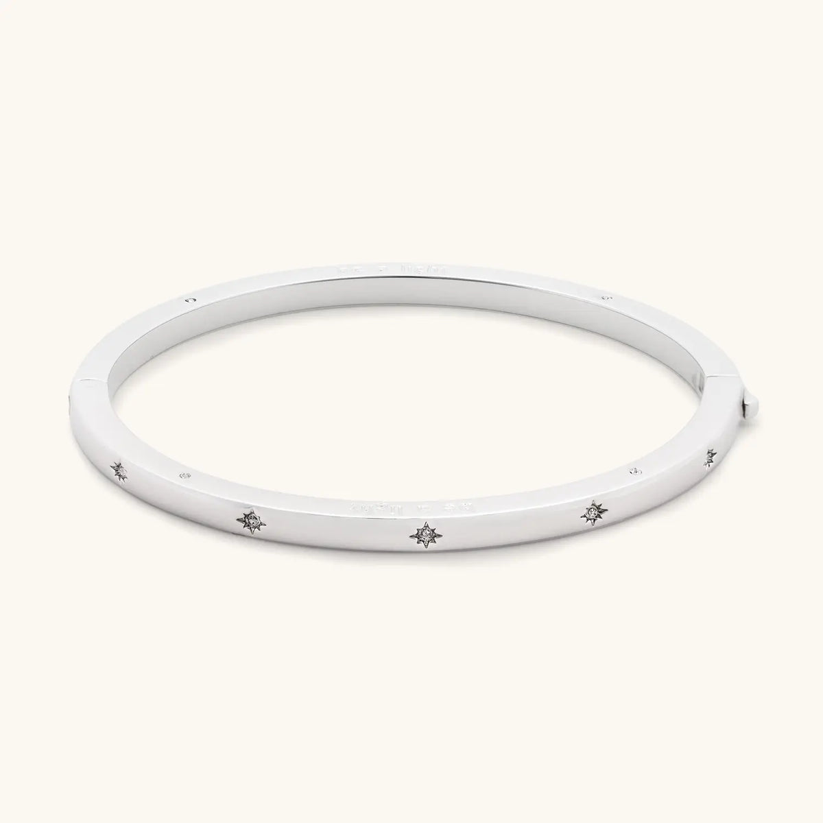 Be A Light Bangle side view, silver-plated bangle with starburst CZ stone details along the outside, detail on cream background
