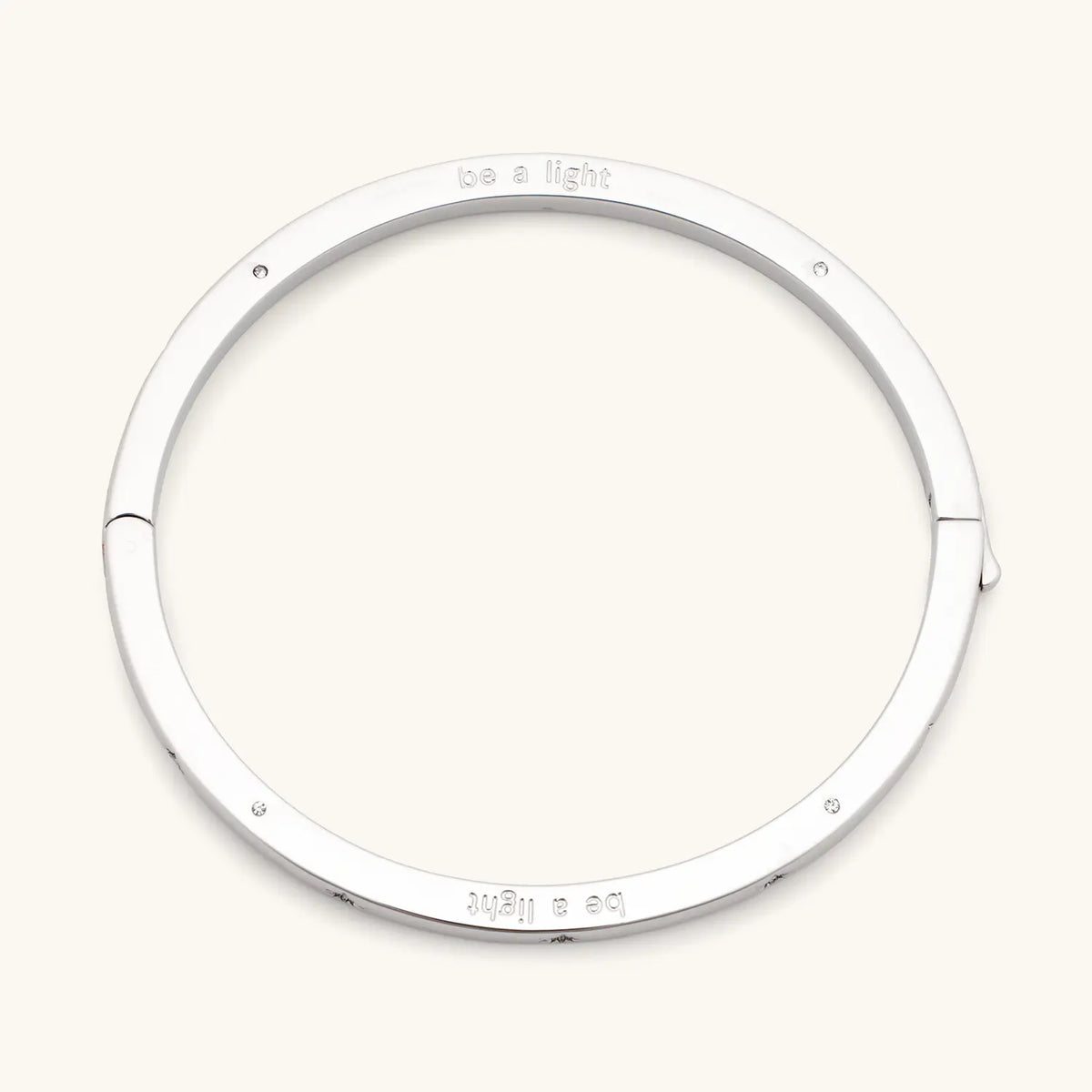 Be A Light Bangle, silver-plated bangle engraved be a light with CZ stone details and push button closure, flat-lay on cream background