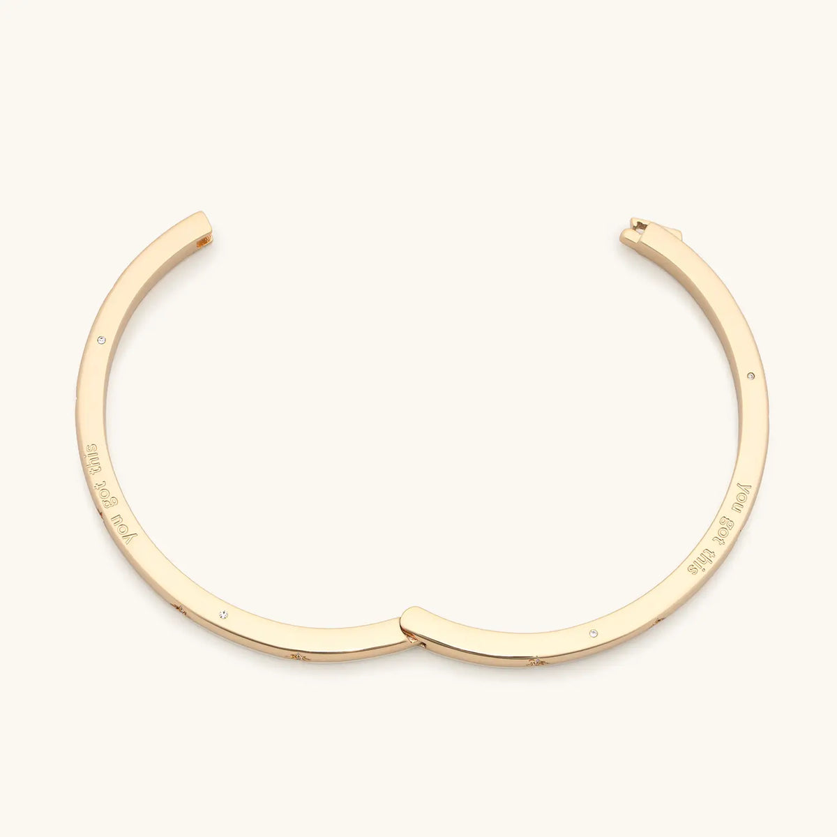 You Got This Bangle open, 18k gold-plated hinged bangle showing you got this engraved on the inside, detail on cream background