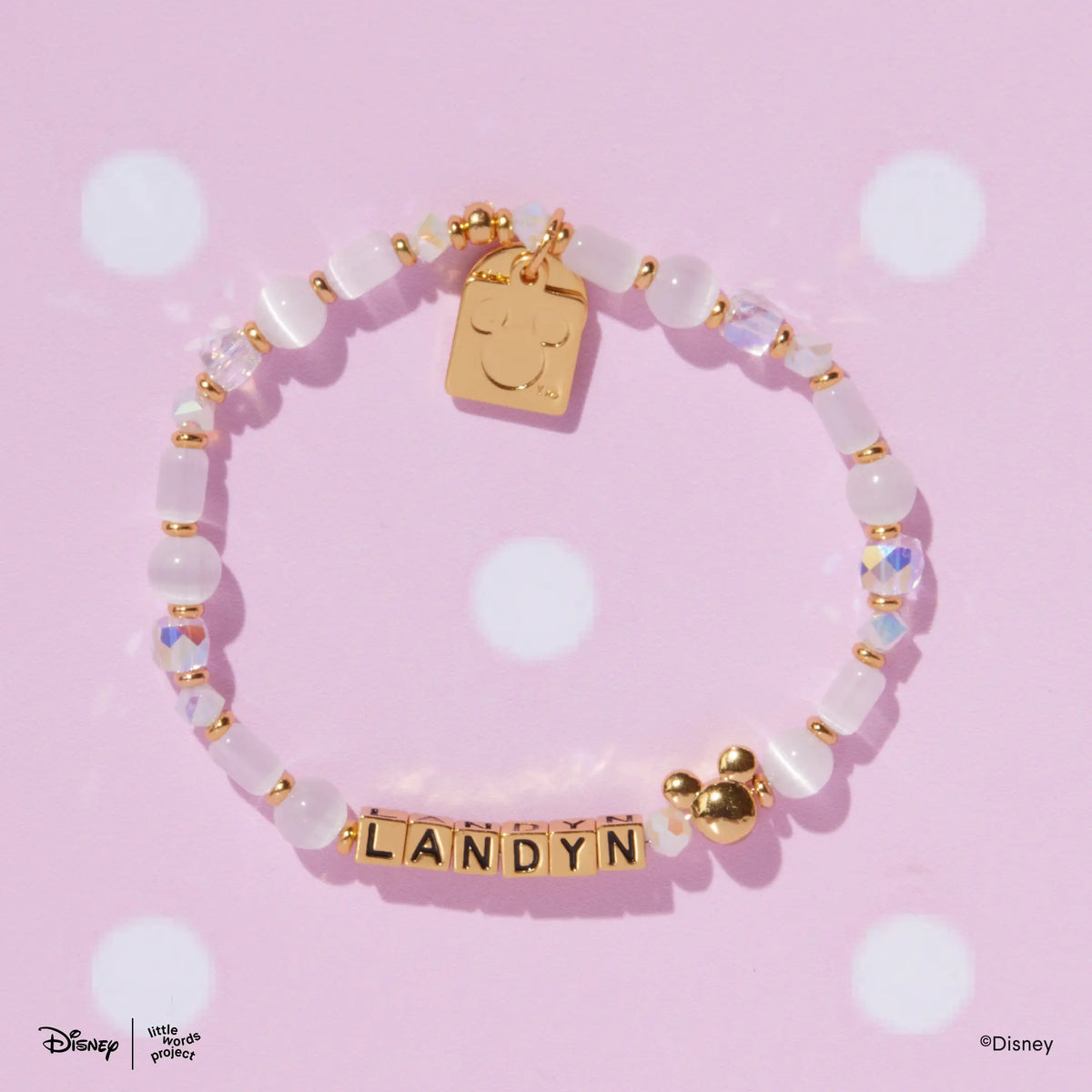 Mickey Custom Magic Maker Disney Mickey & Friends custom bracelet with gold letter beads and a gold plated Mickey Mouse bead, flat lay on pink polka dot background