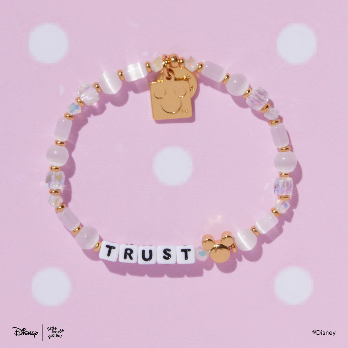 Mickey Custom Magic Maker Disney Mickey & Friends custom bracelet with white letter beads and a gold plated Mickey Mouse bead, flat lay on pink polka dot background