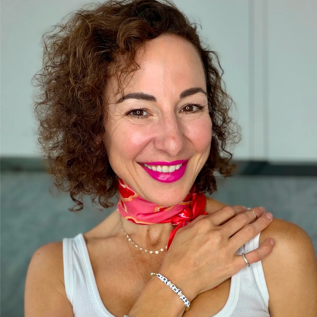 Sarrah Strimel Bentley smiling in a white tank and pink and red silk neck scarf, wearing her Mine the Joy bracelet with her hand resting on her shoulder, on-model portrait