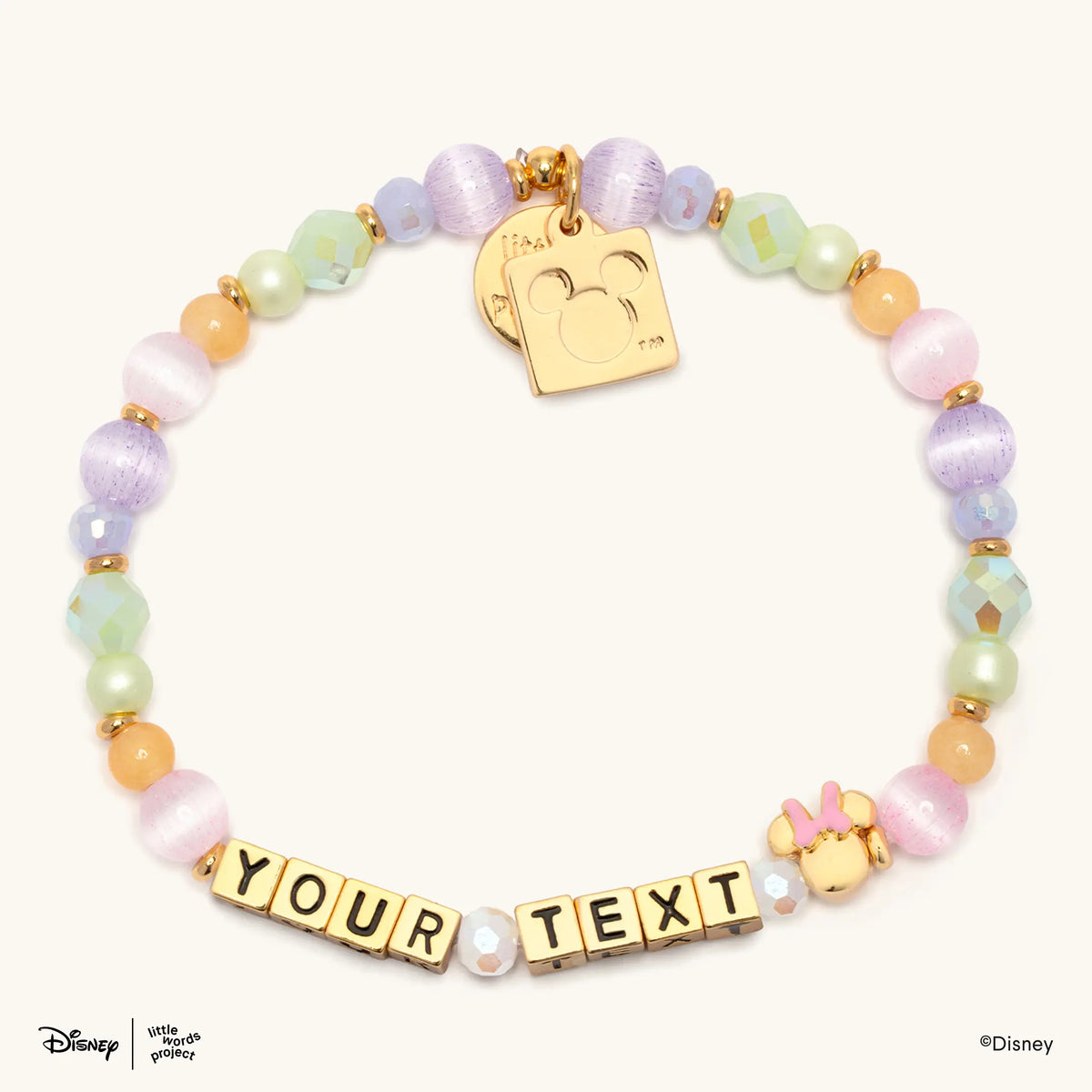Minnie Custom Dot Darling Disney Mickey & Friends custom bracelet with gold letter beads spelling YOUR TEXT, pastel lavender and pink cat's eye beads, mint and lavender iridescent crystals, pale green pearls, peach beads, a gold plated Minnie Mouse bead with a pink bow, and gold Little Words Project and Mickey Mouse logo tags, flat lay