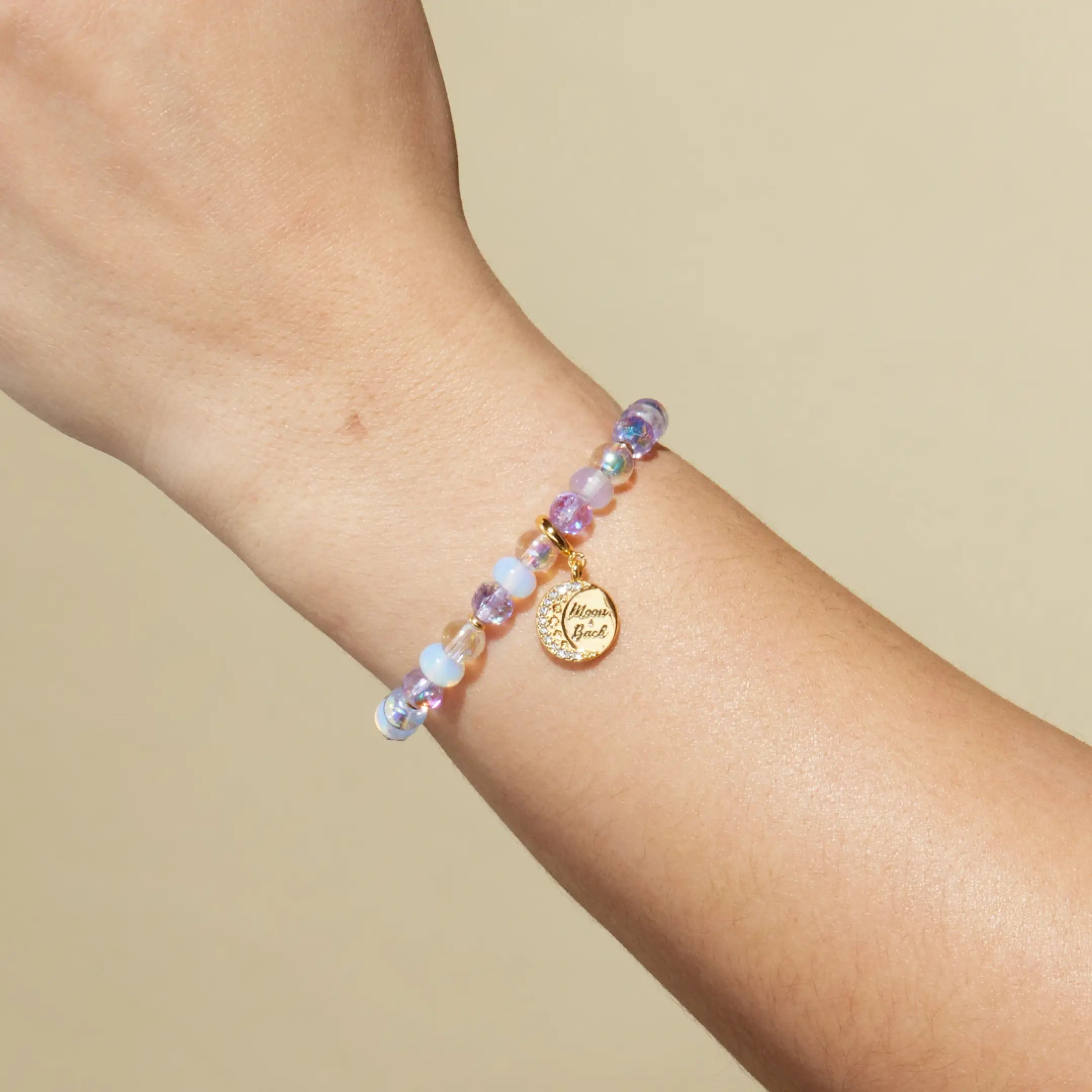 Multicolored beaded bracelet with a gold charm on a wrist against a beige background