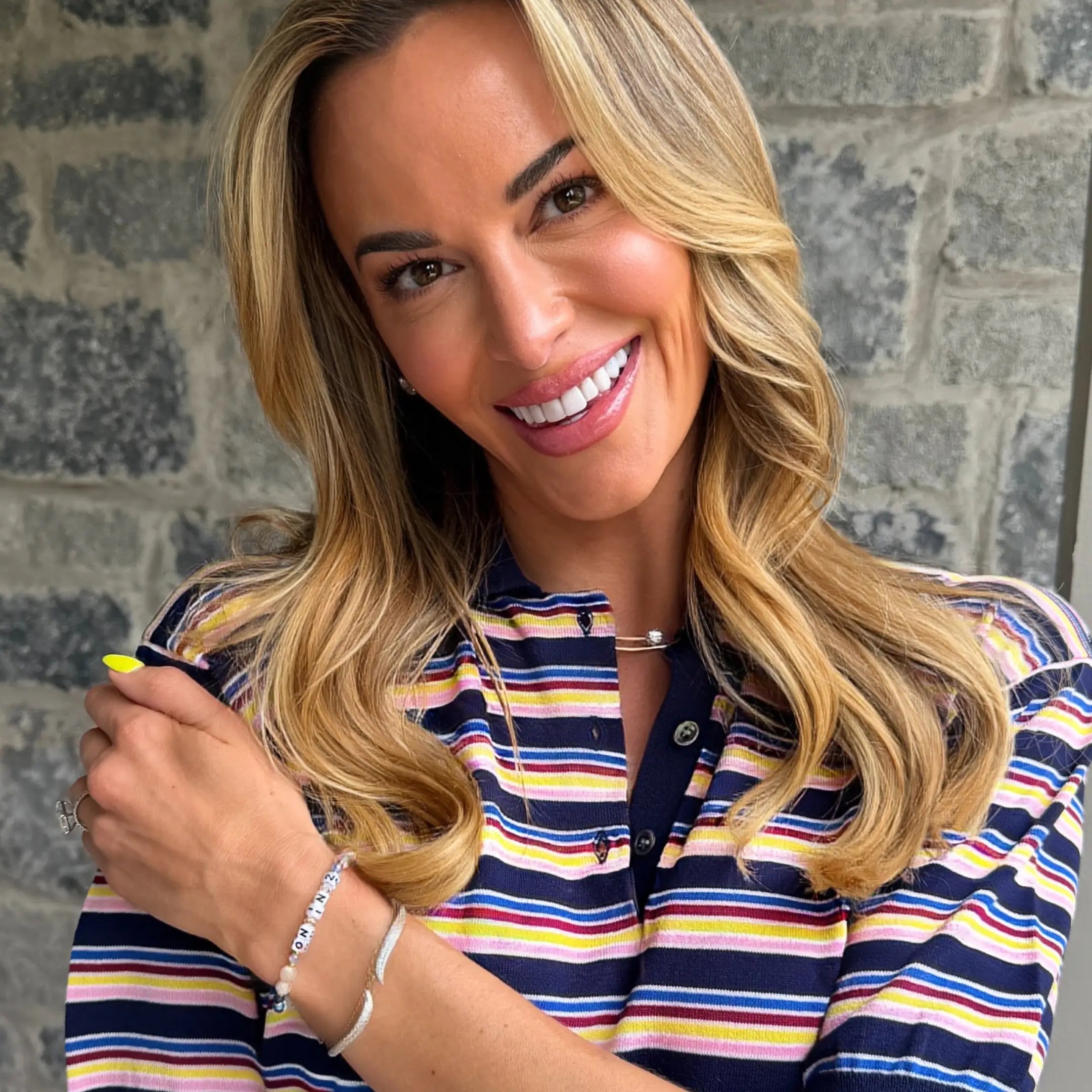 Jena Sims smiling on-model portrait wearing On In 2 LWP bracelet, striped top, stone wall background