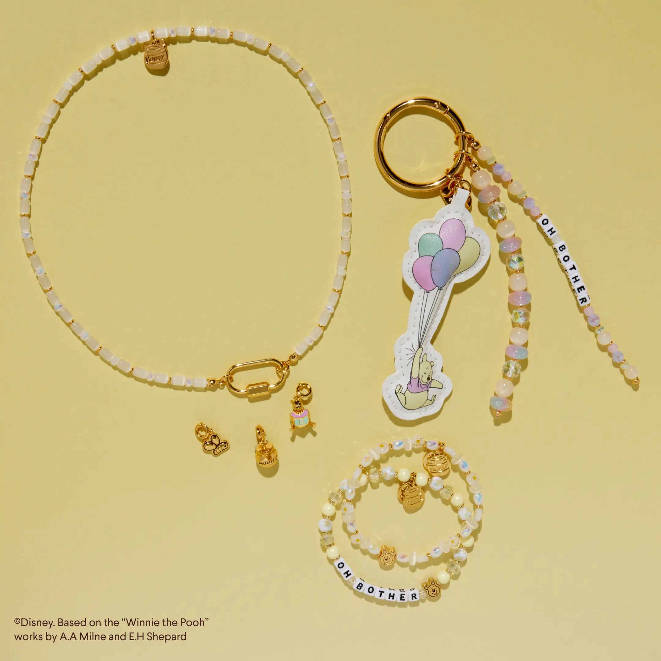 Collection of Winnie the Pooh-themed jewelry and bag charm on a yellow background