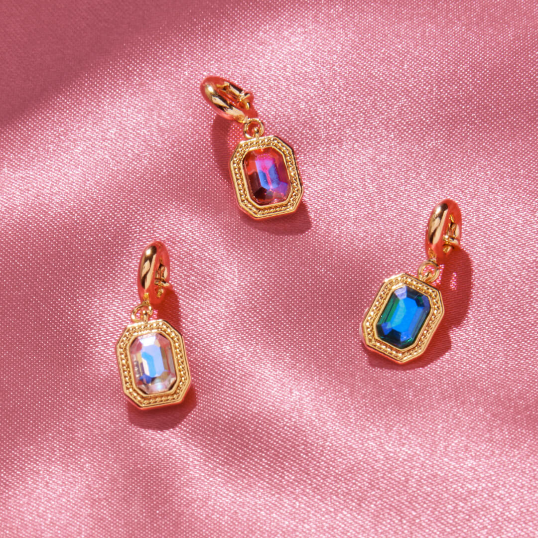 Gold charms with colorful gemstones on a pink fabric background