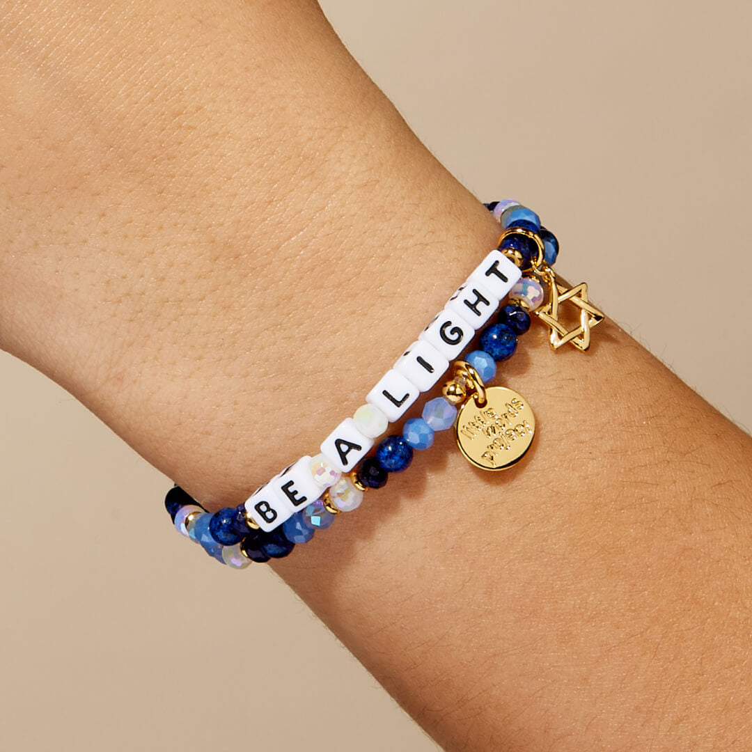 Bracelet with 'Be a Light' message and star of david charm on wrist against beige background
