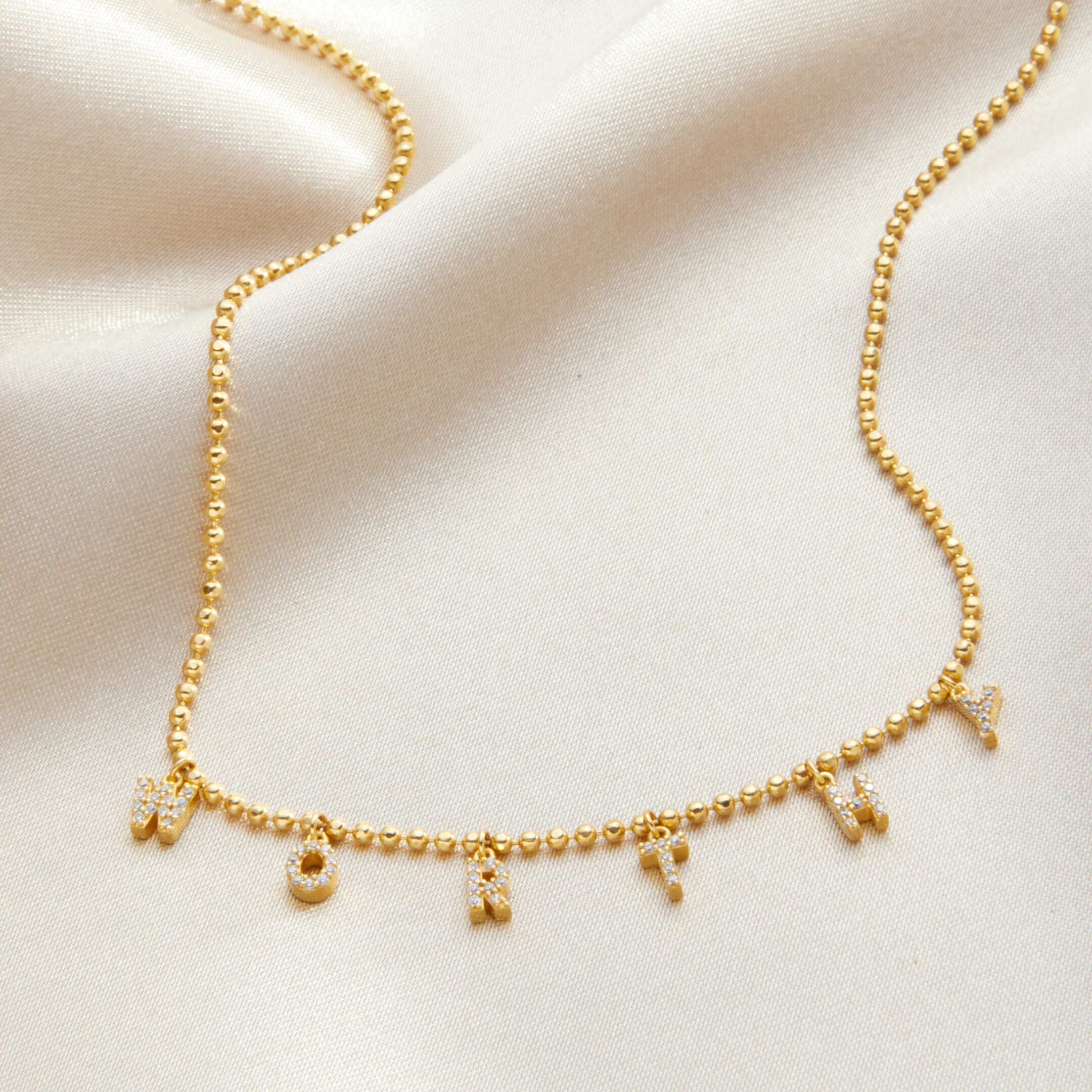 Gold necklace with letter charms on a beige fabric background