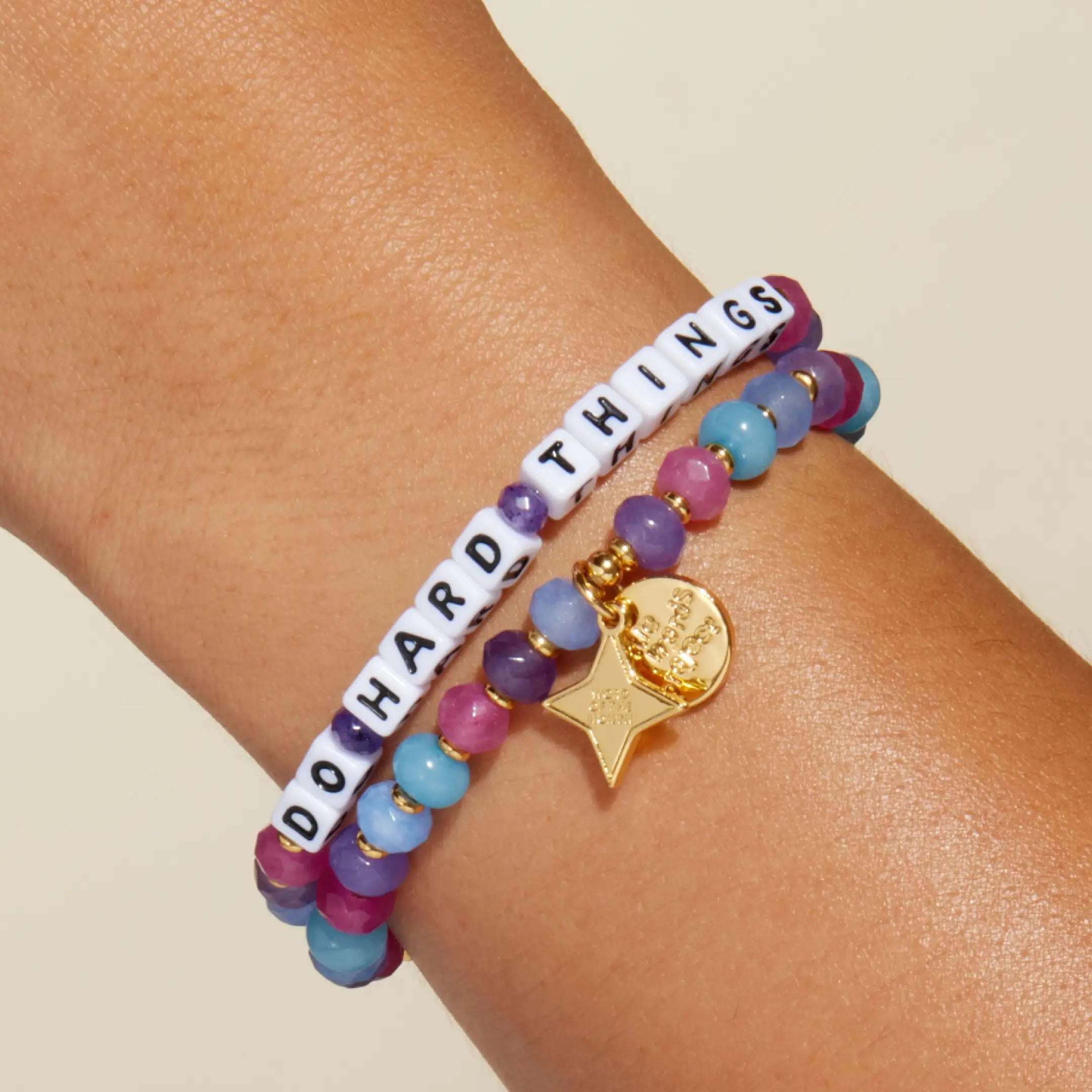 Do Hard Things September Word of the Month bracelet with white letter beads worn on a wrist and stacked with a matching pink, purple and blue beaded bracelet