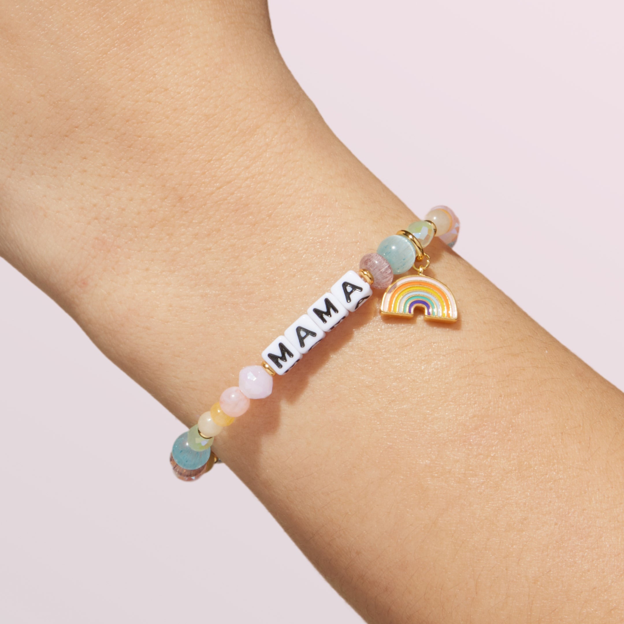 Bracelet with 'MAMA' and a rainbow charm on wrist against a light background