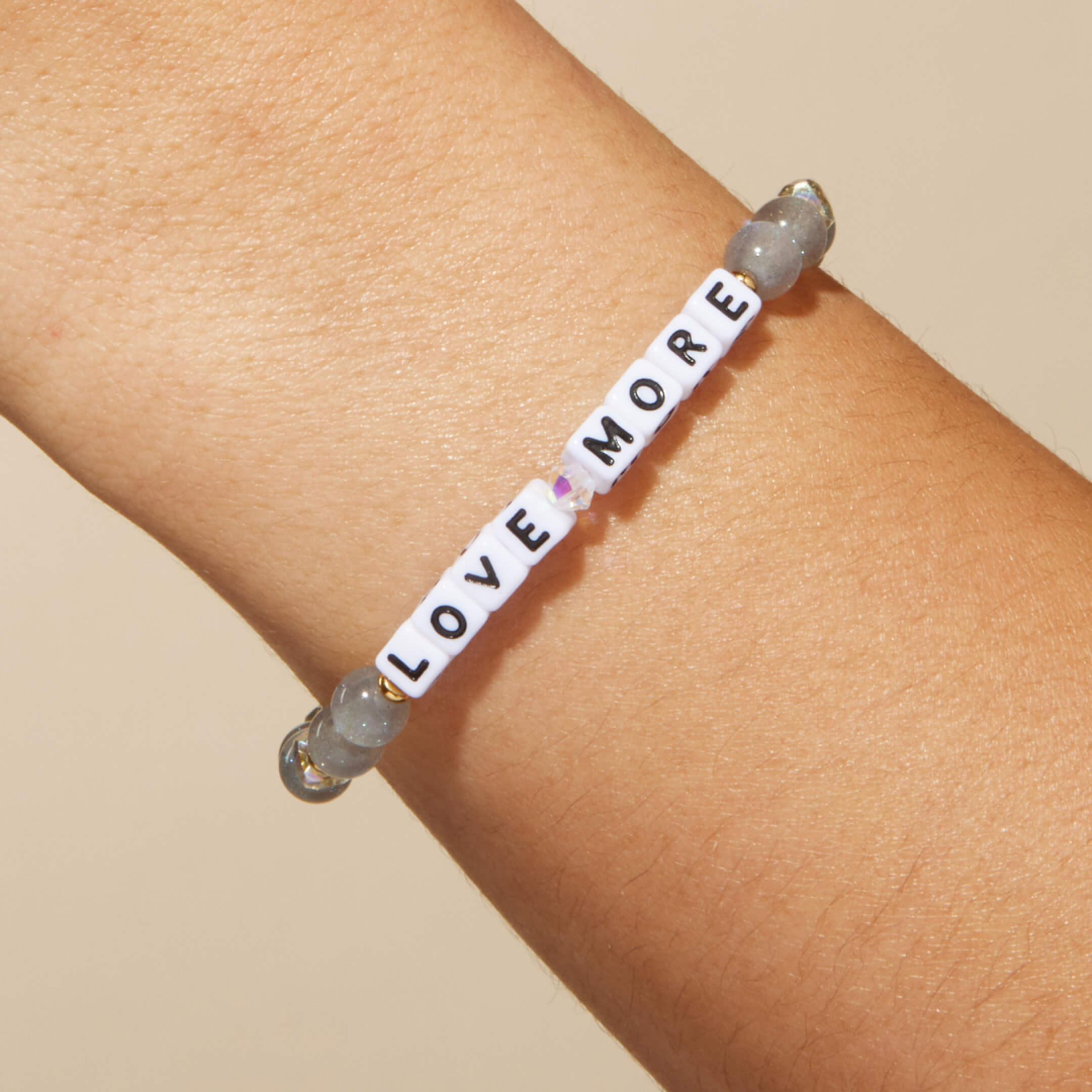 Bracelet with 'LOVE MORE' beads on a wrist against a beige background