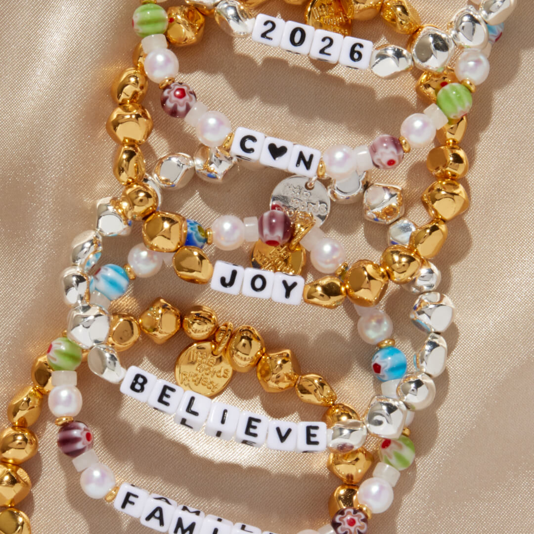 Stack of colorful beaded bracelets with inspirational charms on a beige background