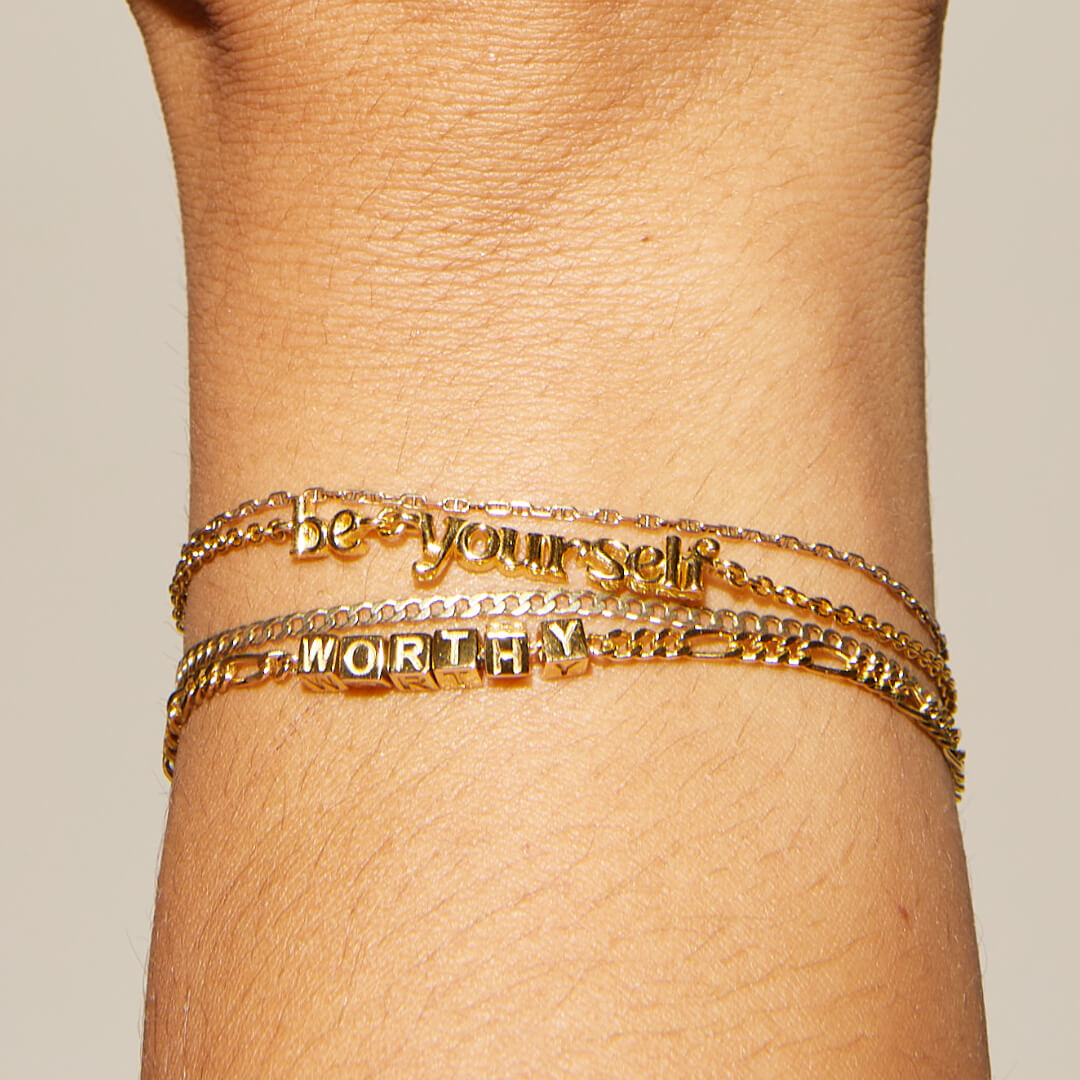 Gold bracelet with motivational text on a wrist against a beige background