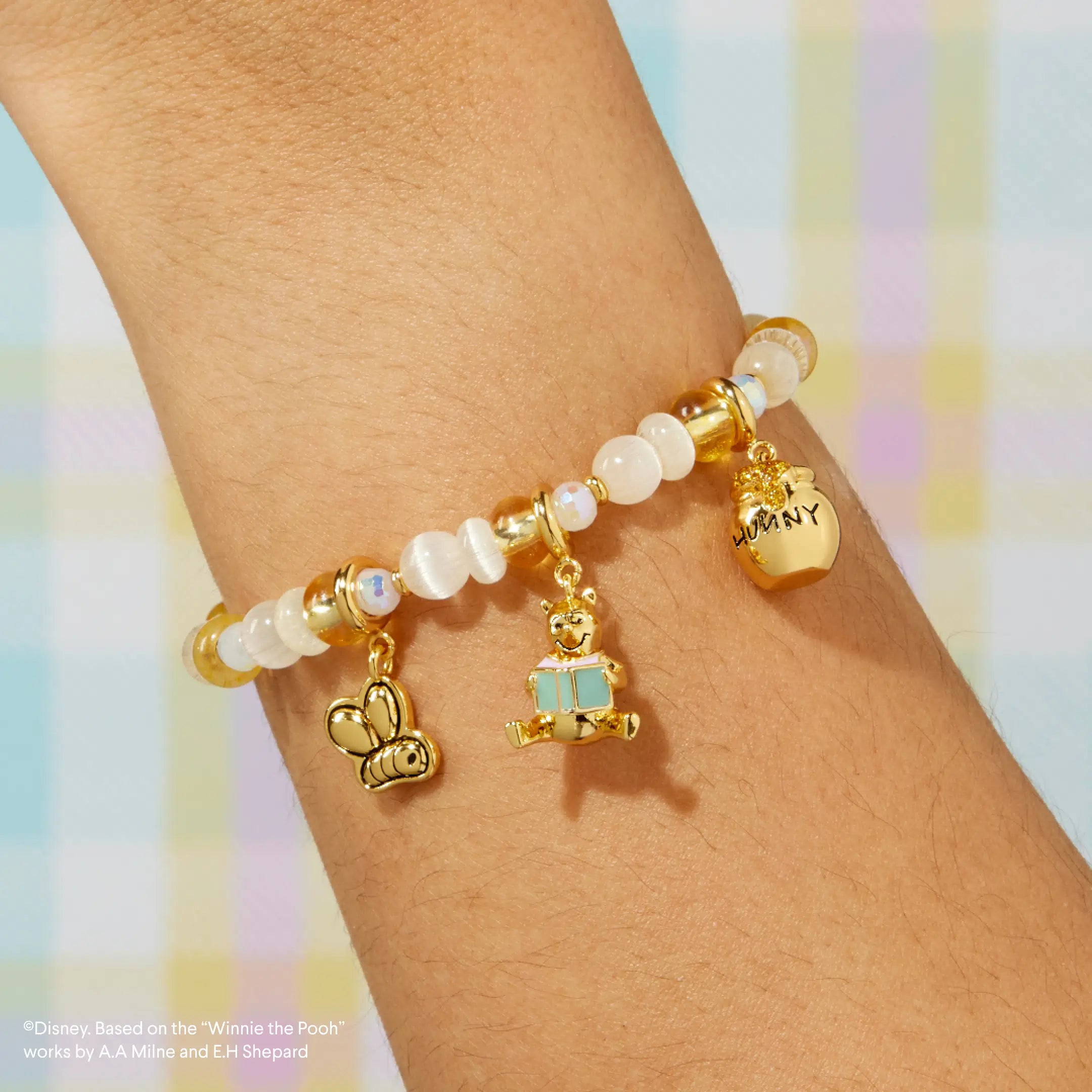 Bracelet with 3 charms on a wrist against a pastel background