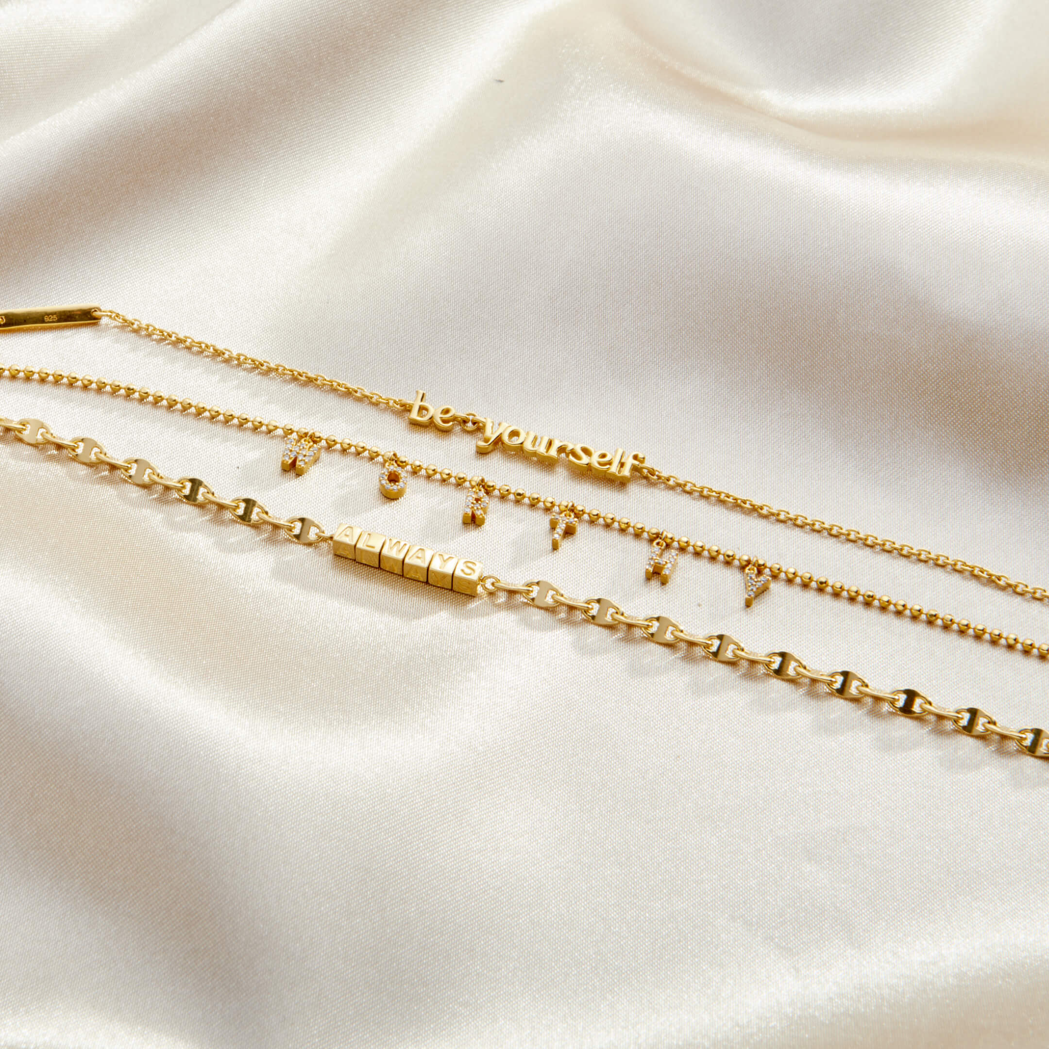 Three gold necklaces on a soft beige fabric background