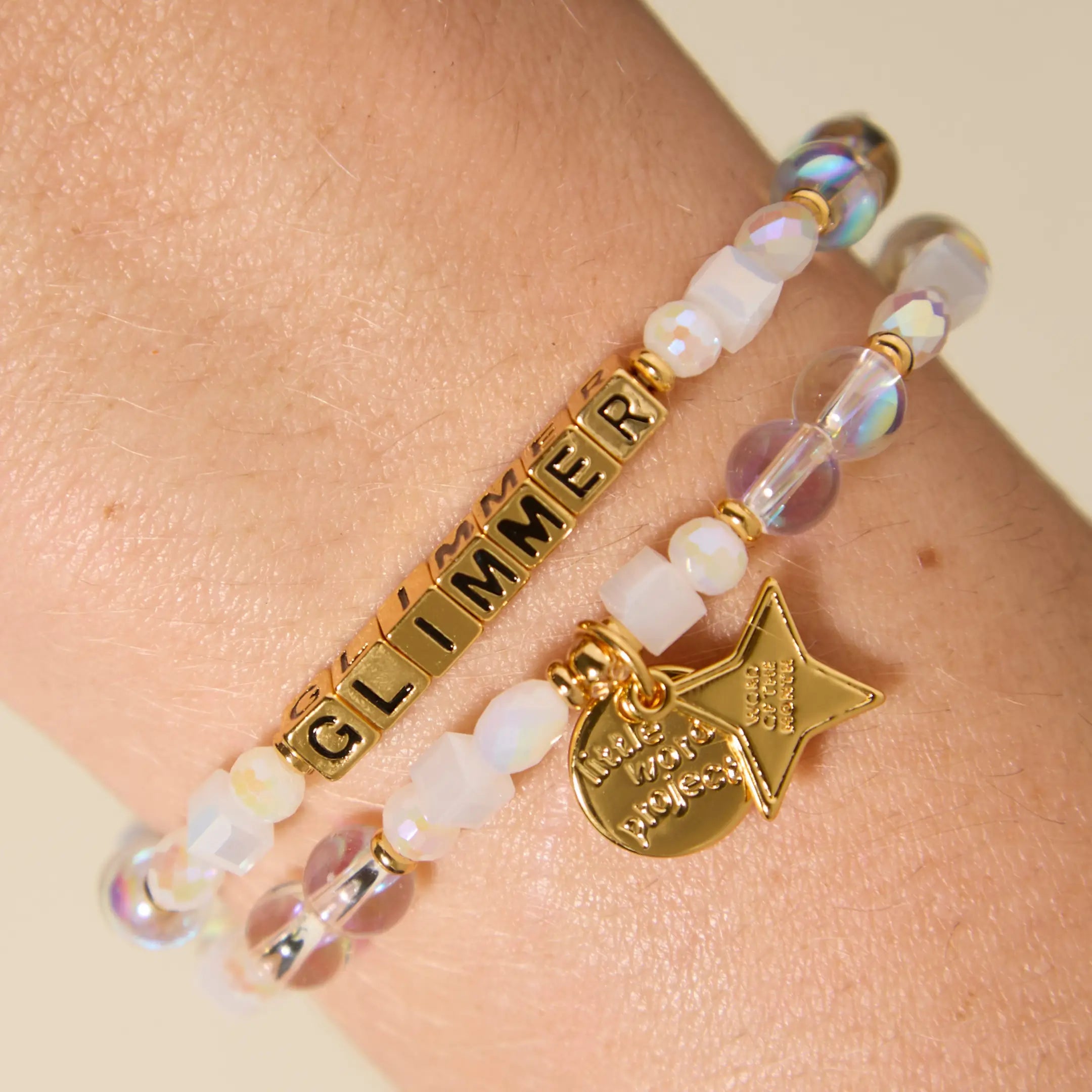 Bracelet with 'Glimmer' charm on wrist against beige background