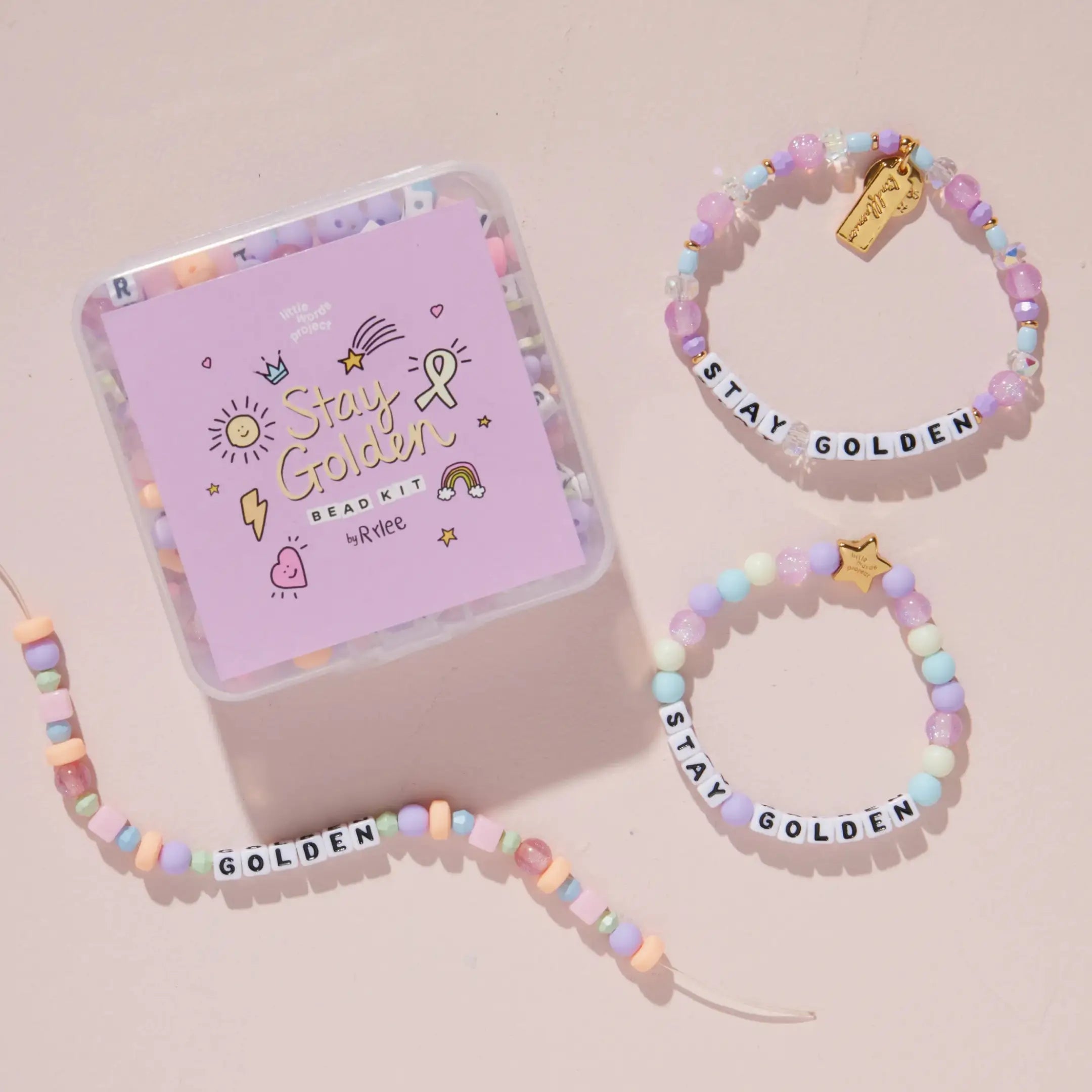 Stay Golden Bead Kit Set Rylee Ta styled with purple bead kit box, gold letter bead bracelet and kids bracelet on a blush pink background