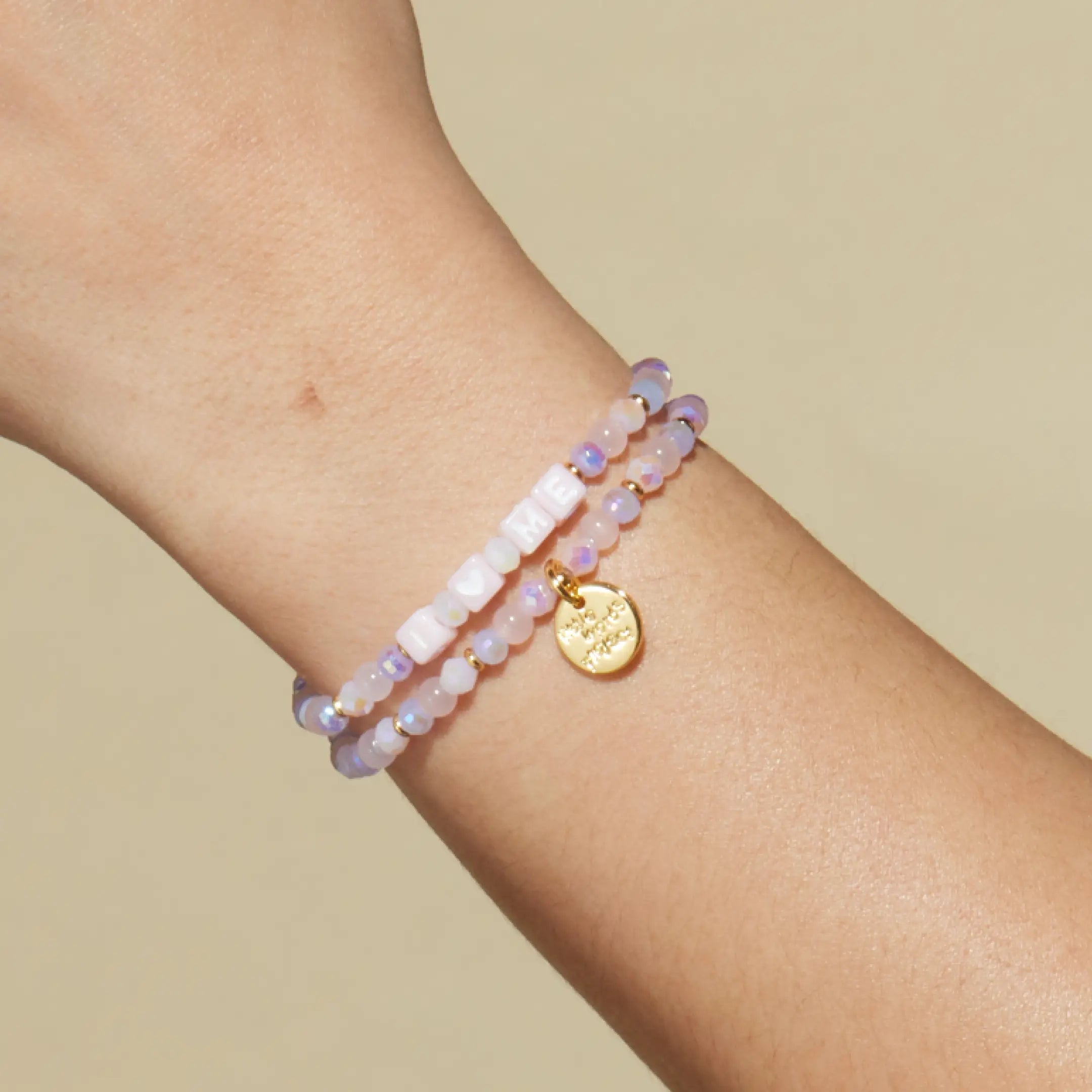 Beaded bracelet with a gold charm on a wrist against a beige background