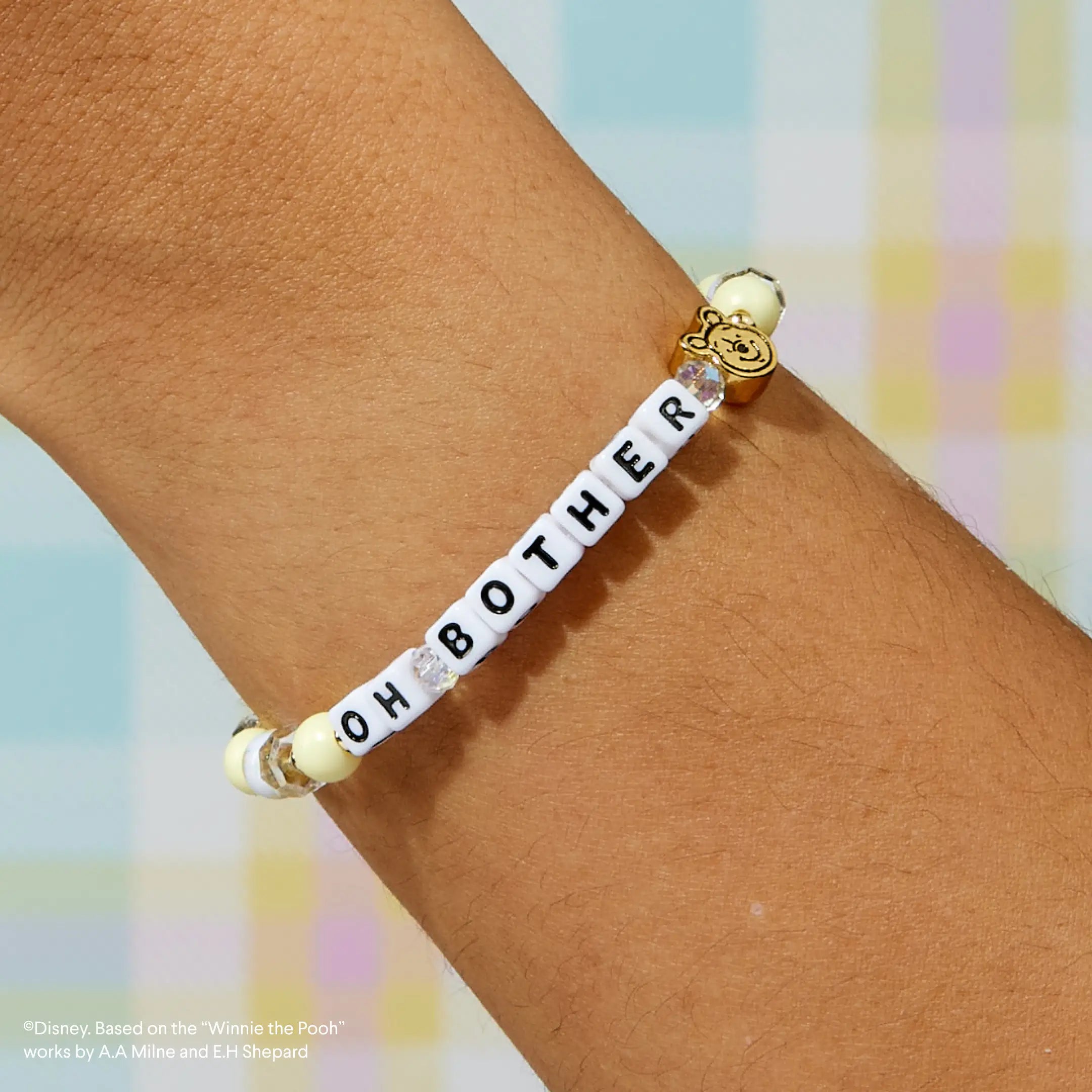 Bracelet with letter beads spelling 'Oh Bother' on a wrist against a pastel background