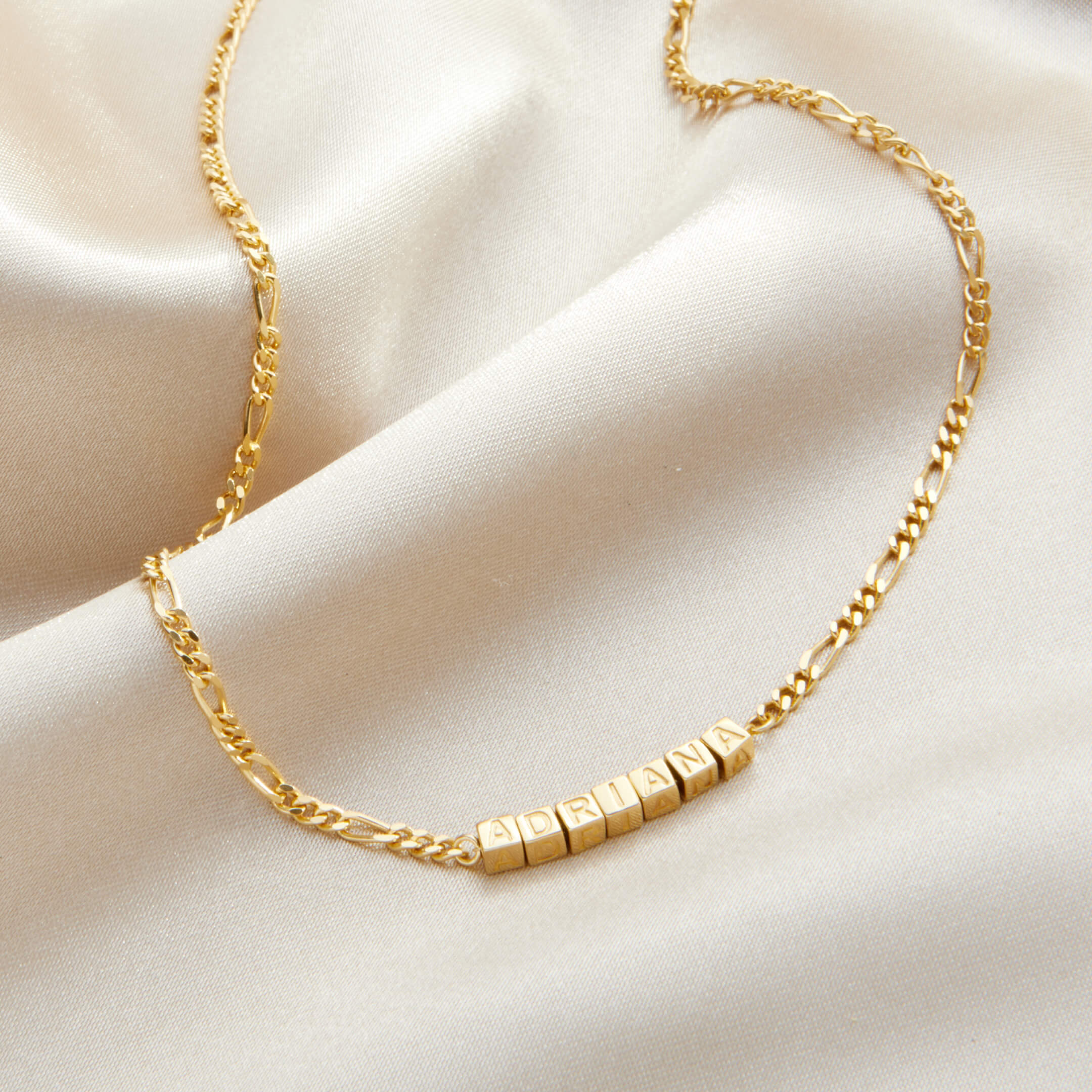 Gold necklace with cube-shaped beads on a beige fabric background