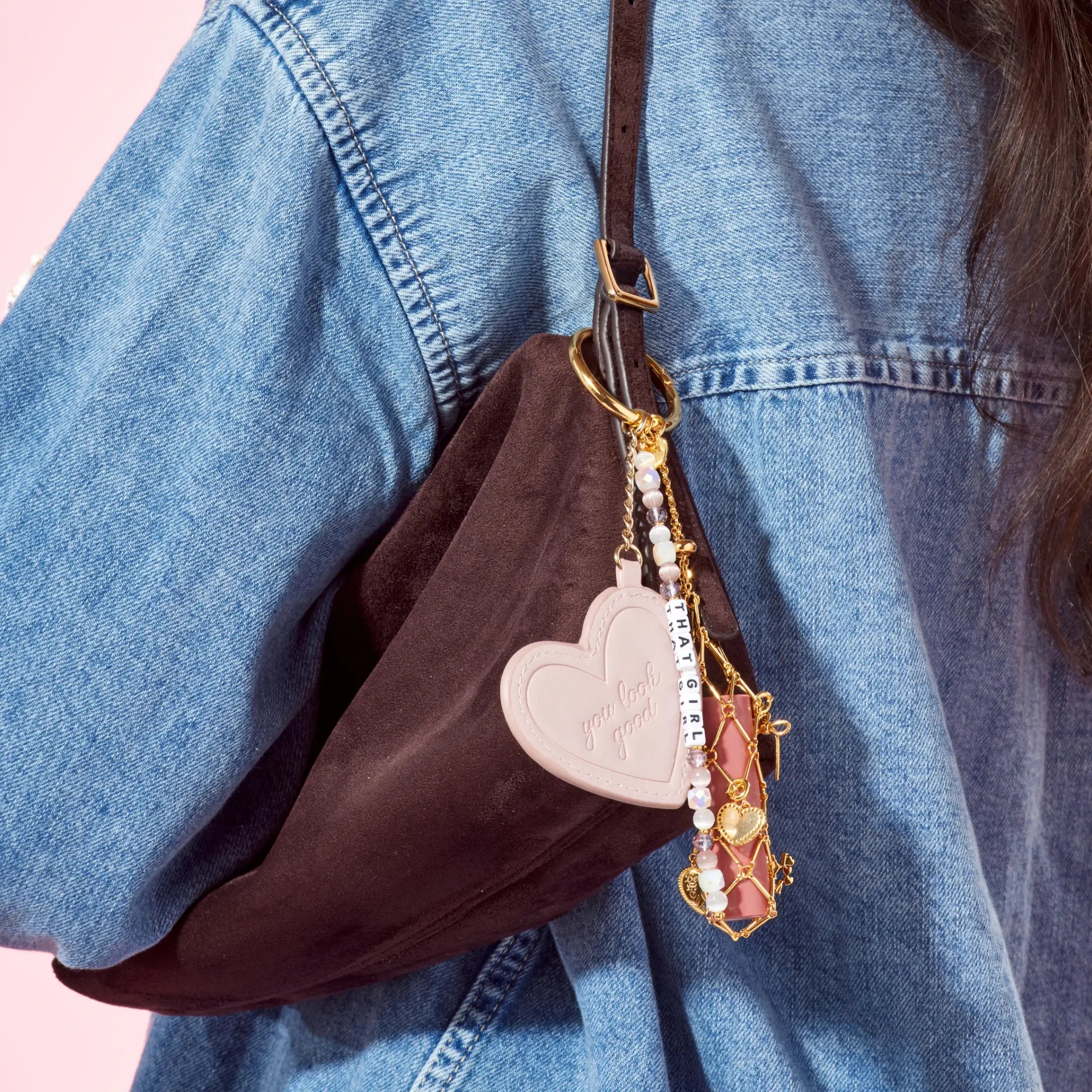 Brown bag with heart-shaped keychain and decorative elements worn by a person in a denim jacket.