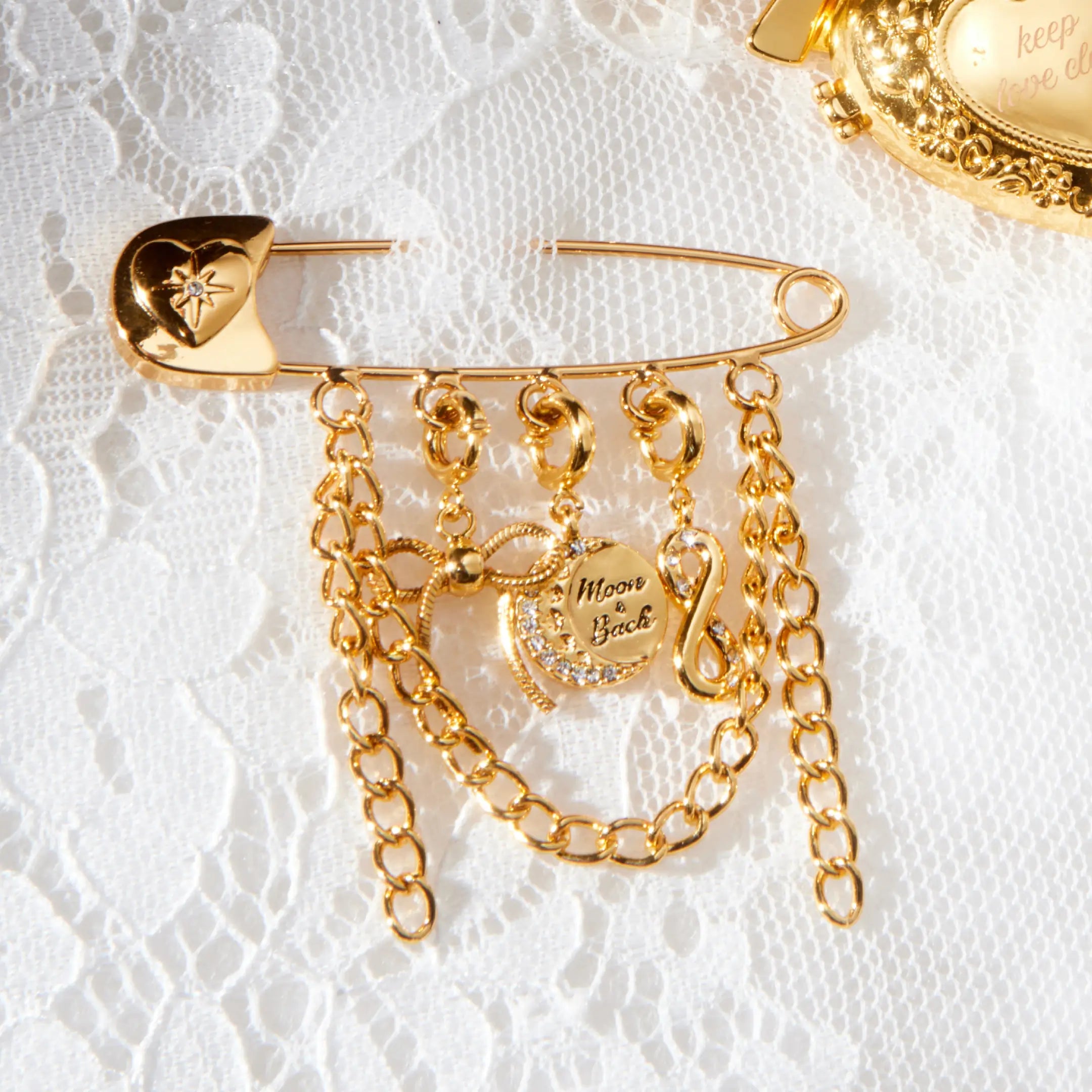 Gold safety pin with chains and charms on a white lace background