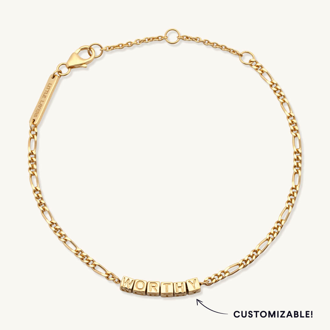 Gold bracelet with 'WORTHY' charm on a white background