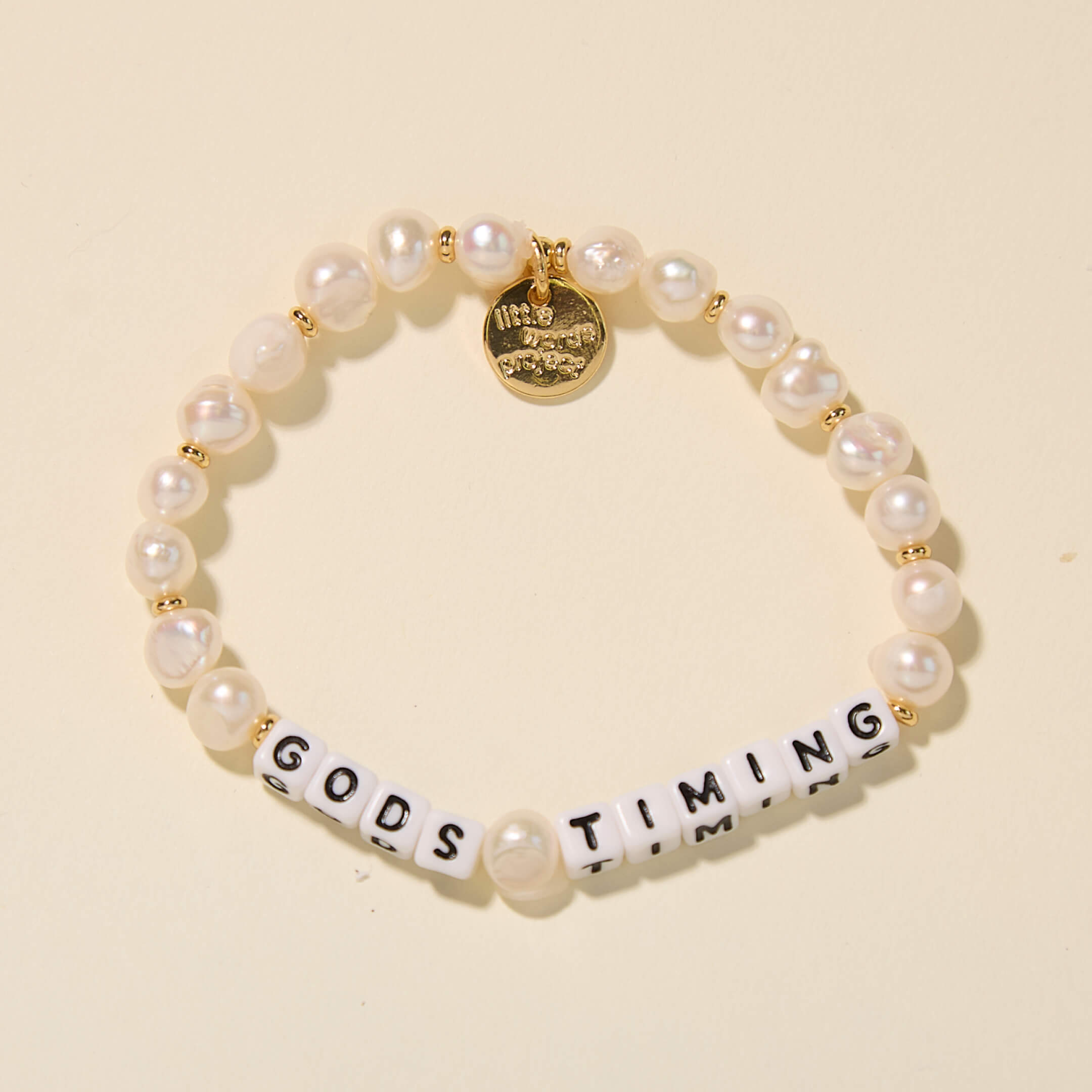 Pearl bracelet with letter beads spelling 'GODS TIMING' on a beige background