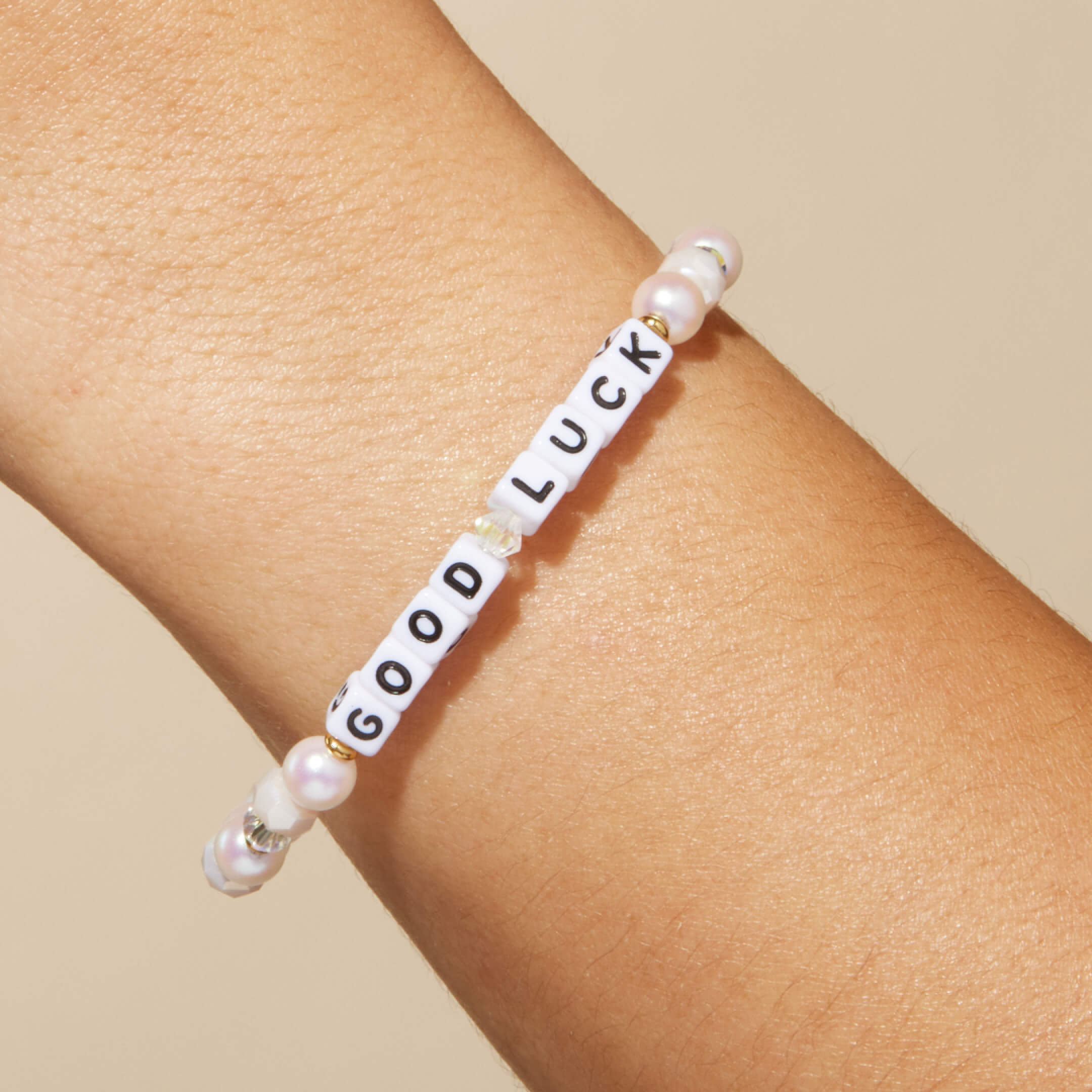 Bracelet with 'GOOD LUCK' beads on a wrist against a beige background