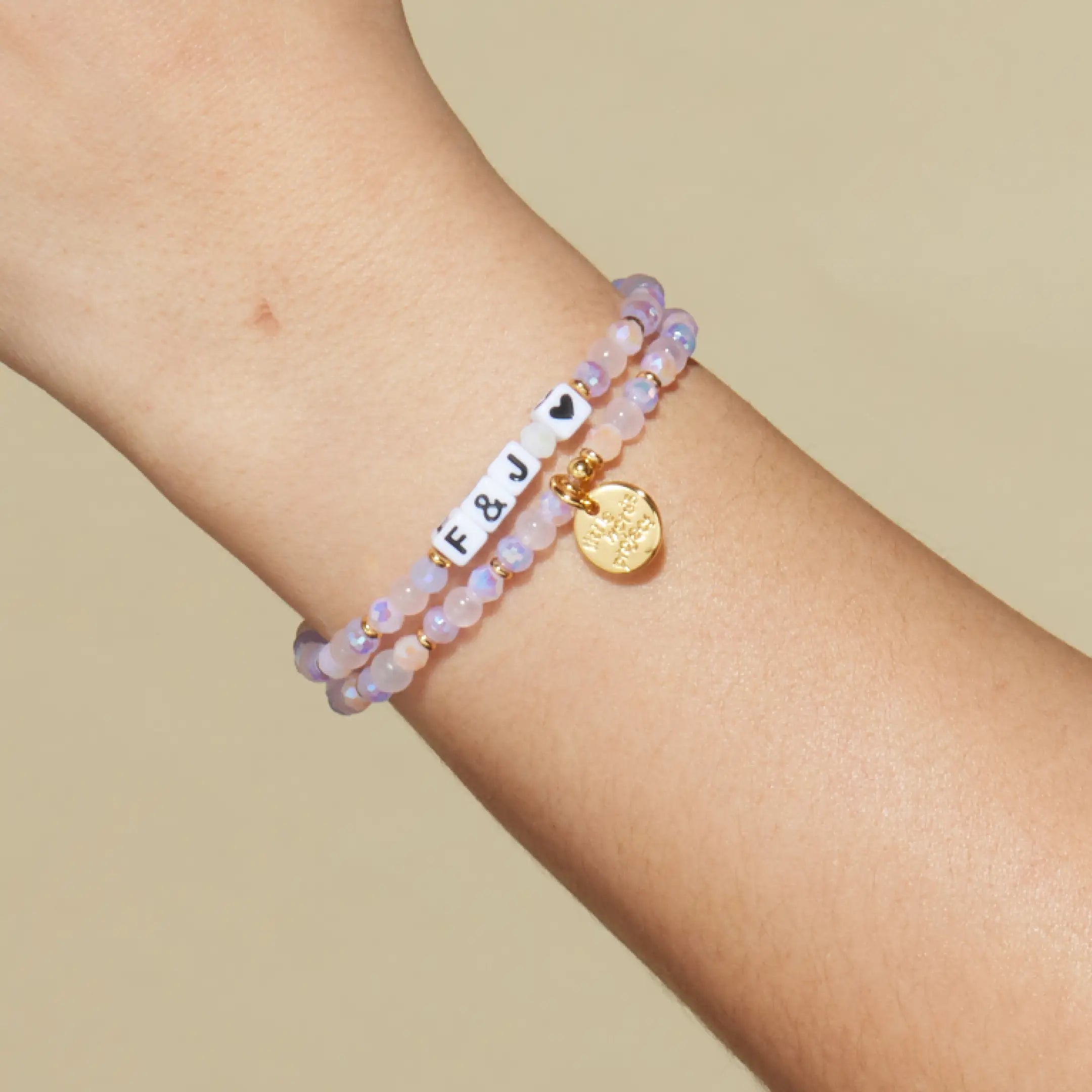 Bracelet with letter beads and a gold tag on a wrist against a beige background
