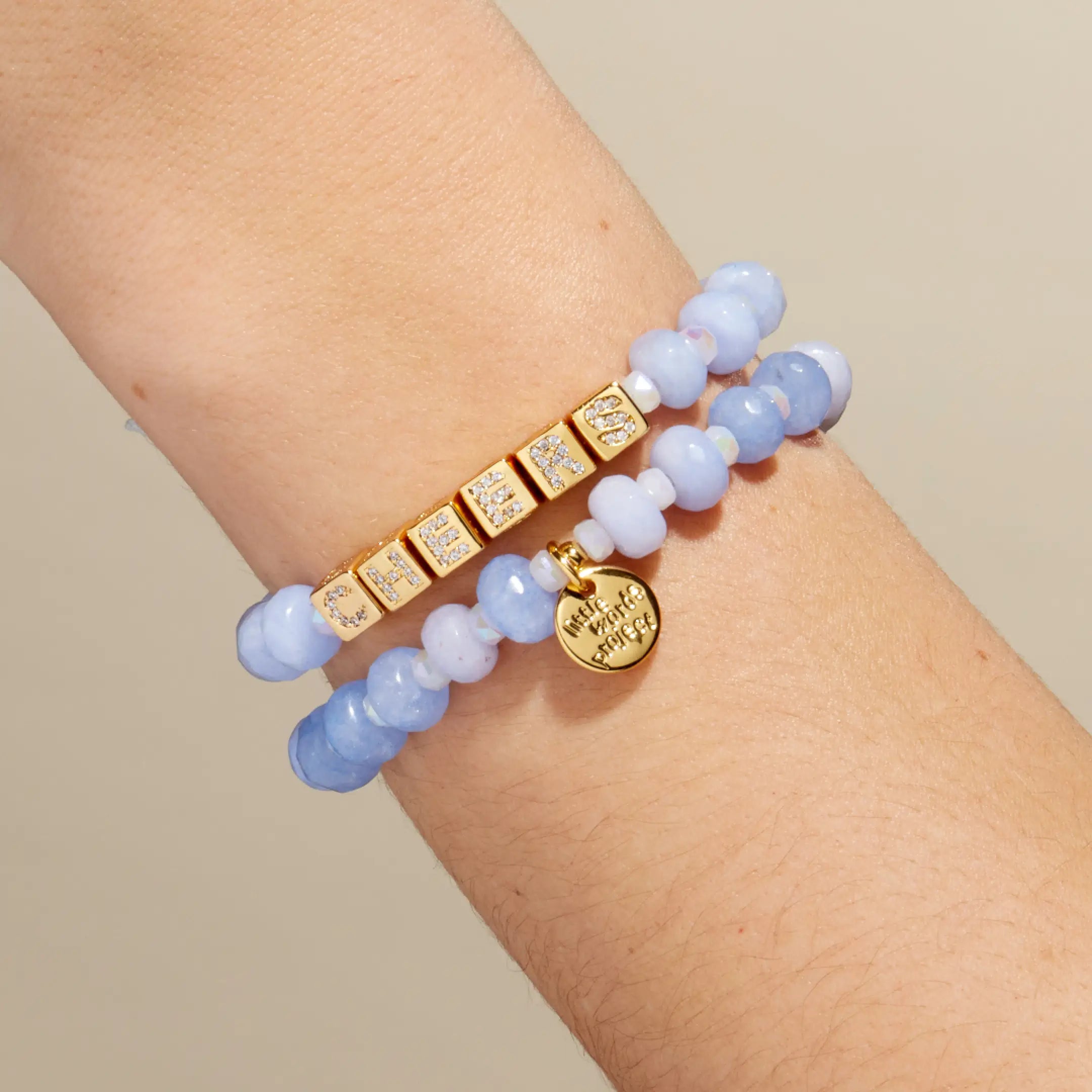 Two bracelets with blue beads and gold accents on a wrist against a beige background