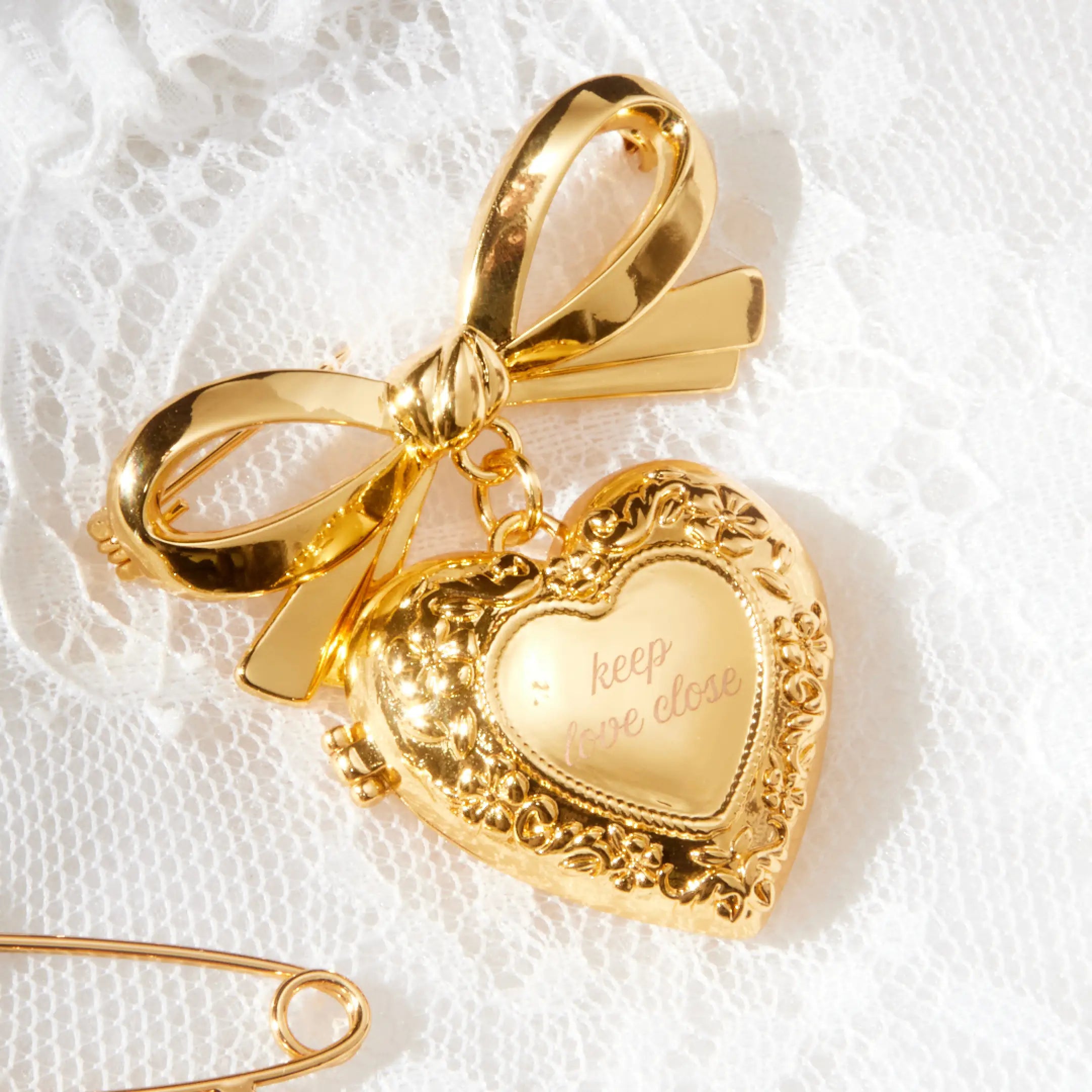 Gold bow-shaped brooch with heart pendant on a white lace background