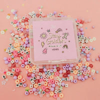 Stay Golden Bead Kit Rylee Ta purple box surrounded by scattered letter beads and pastel pink, purple and yellow beads on a pink background
