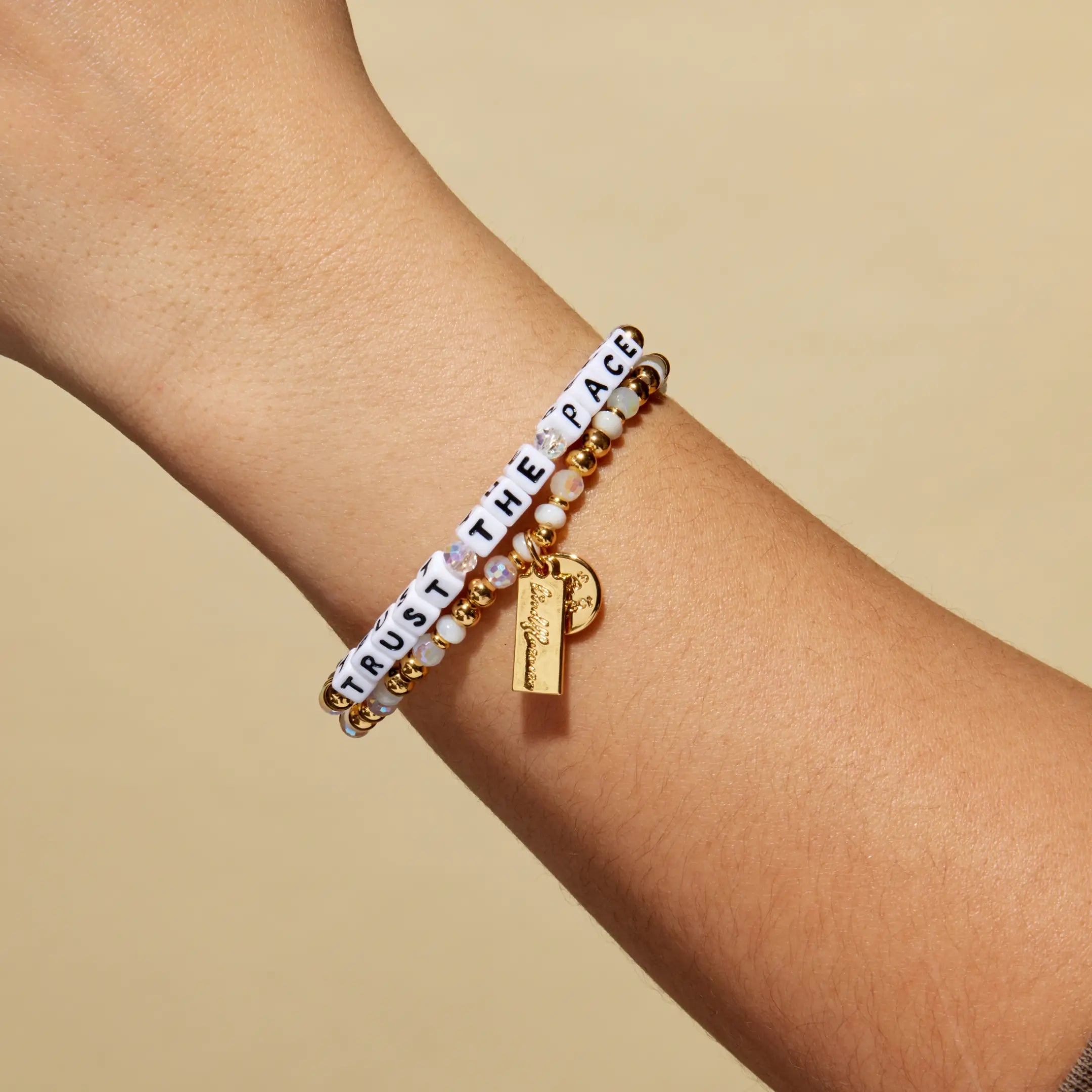 Bracelet with 'Trust the Pace' message on a wrist against a beige background