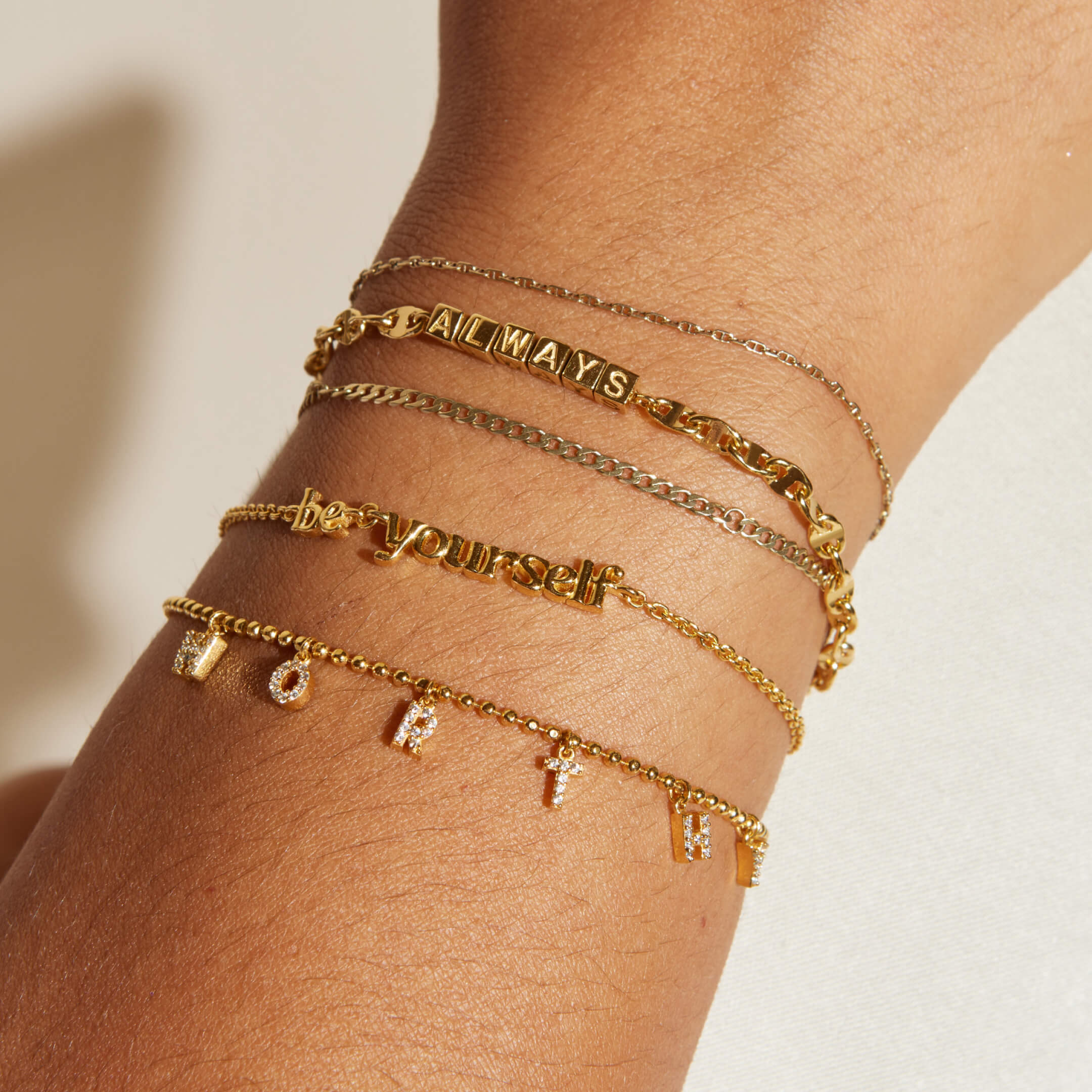 Gold bracelets on a wrist with motivational phrases against a neutral background