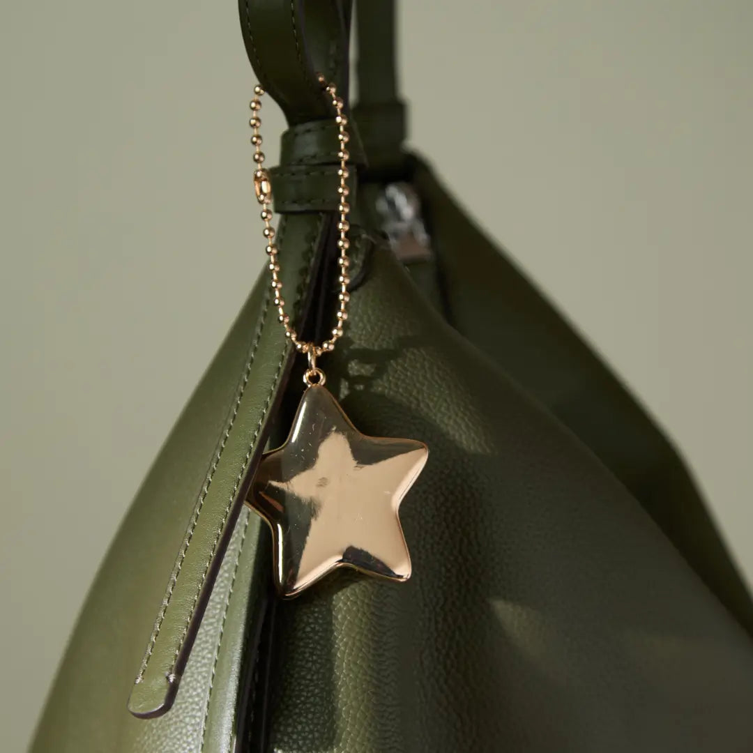 Gold star-shaped pendant on a chain attached to a green bag.