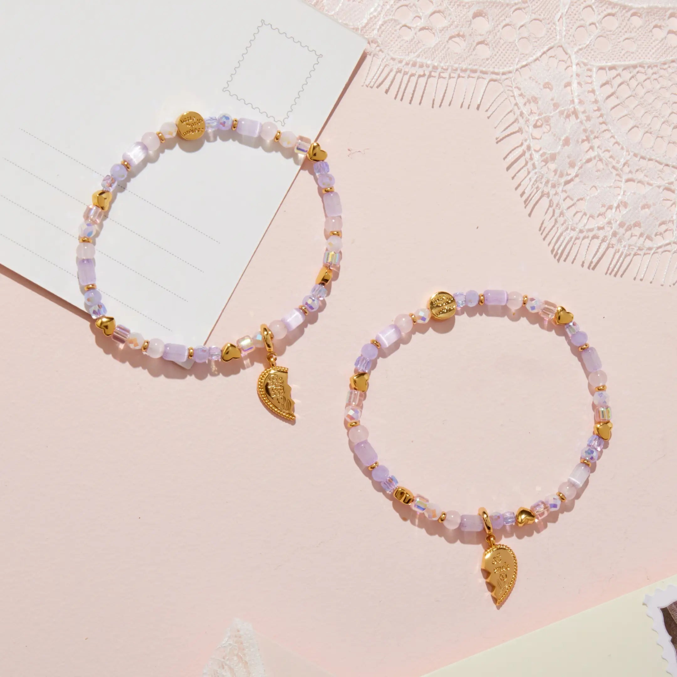 Two beaded bracelets with gold charms on a pink surface
