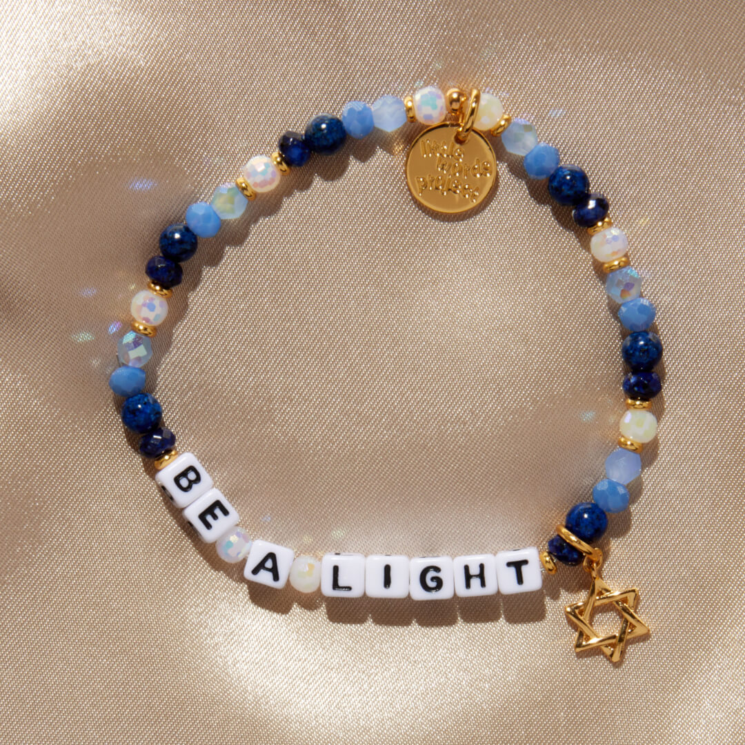 Bracelet with beads, a gold tag, and a Star of David charm on a beige fabric background.