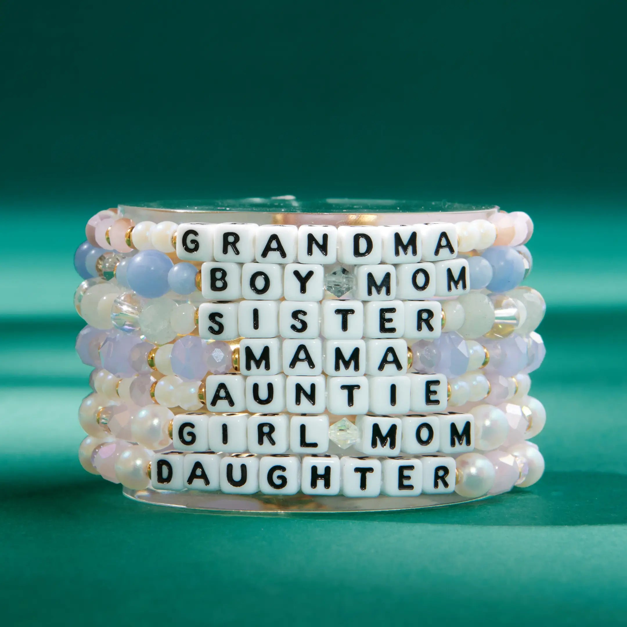 Stack of beaded bracelets with word charms on a green background