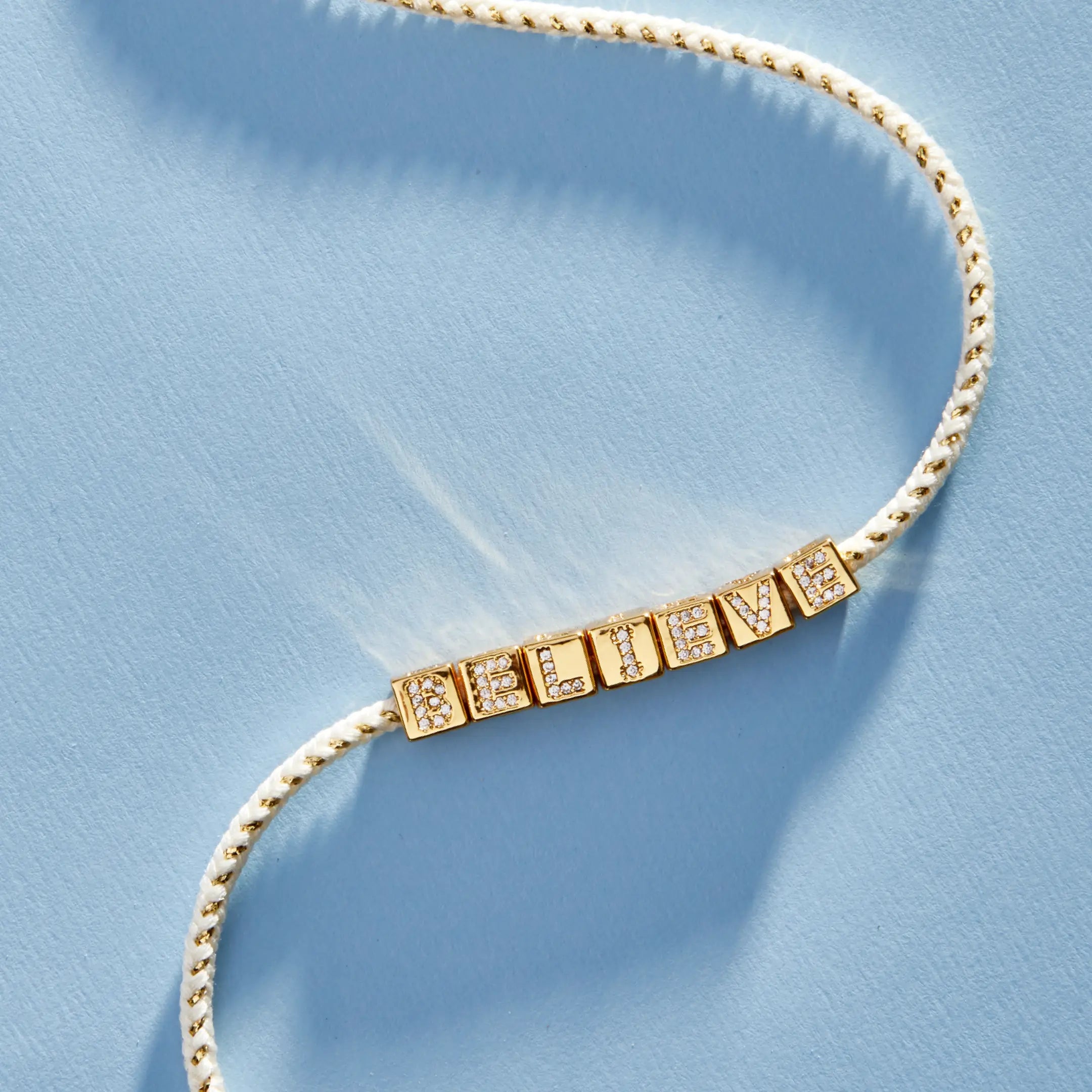 Gold necklace with 'BELIEVE' on a light blue background