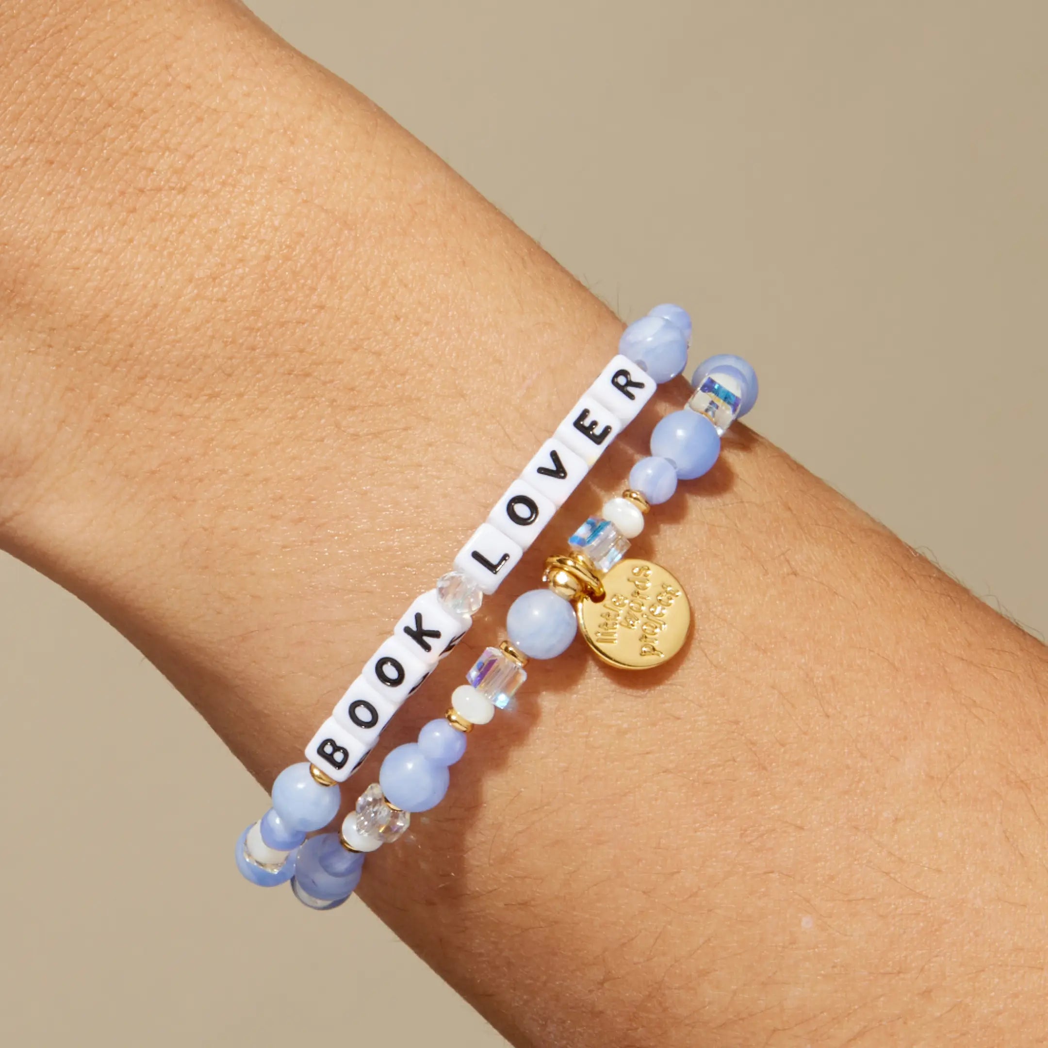 Bracelet with 'BOOK LOVER' beads on a wrist against a beige background