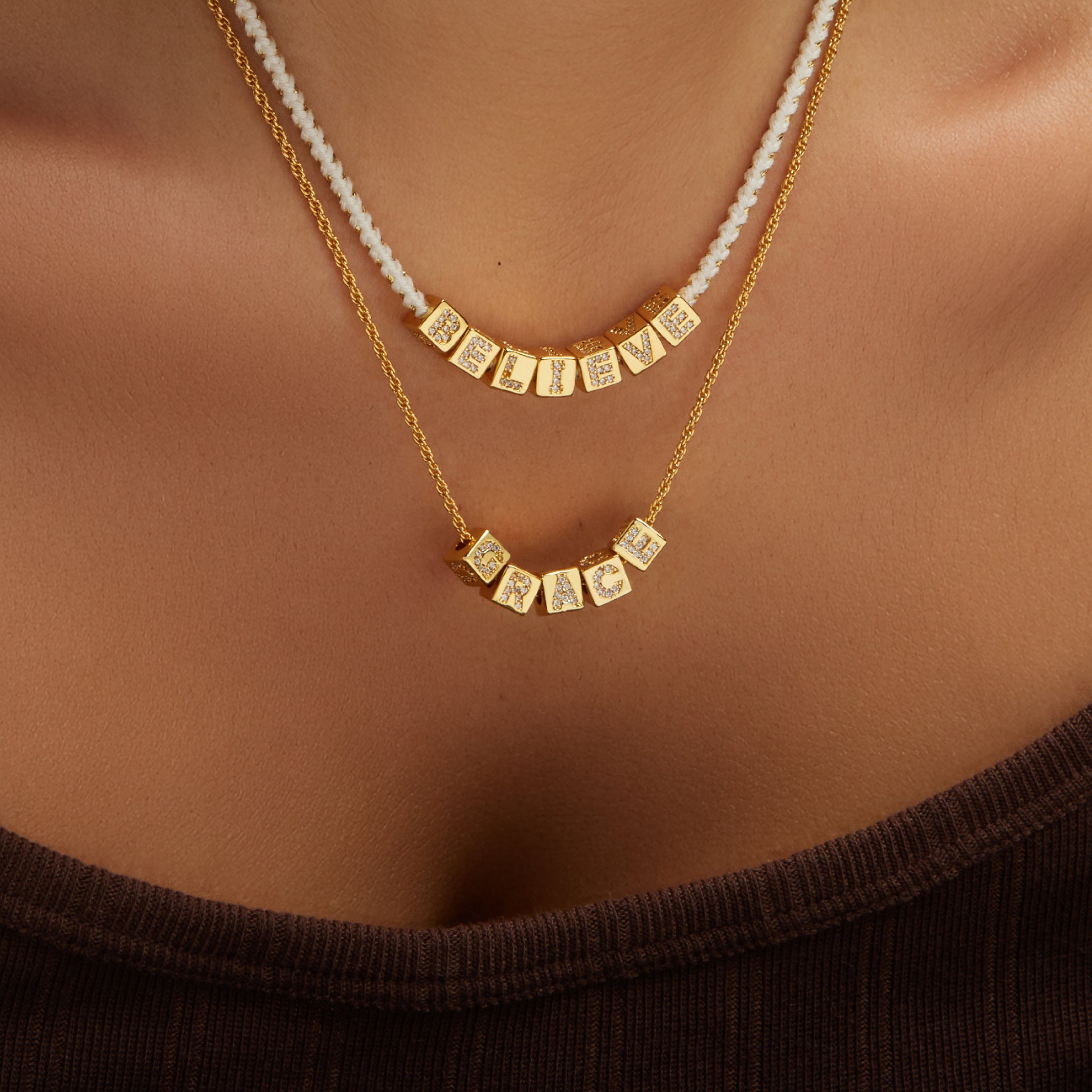 Gold necklaces with square pendants on a person wearing a brown top.