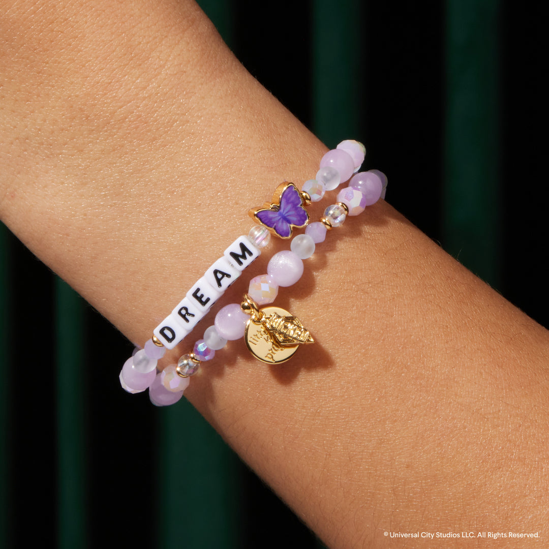 Bracelet with purple beads, butterfly charm, and 'DREAM' bar on wrist against a dark background