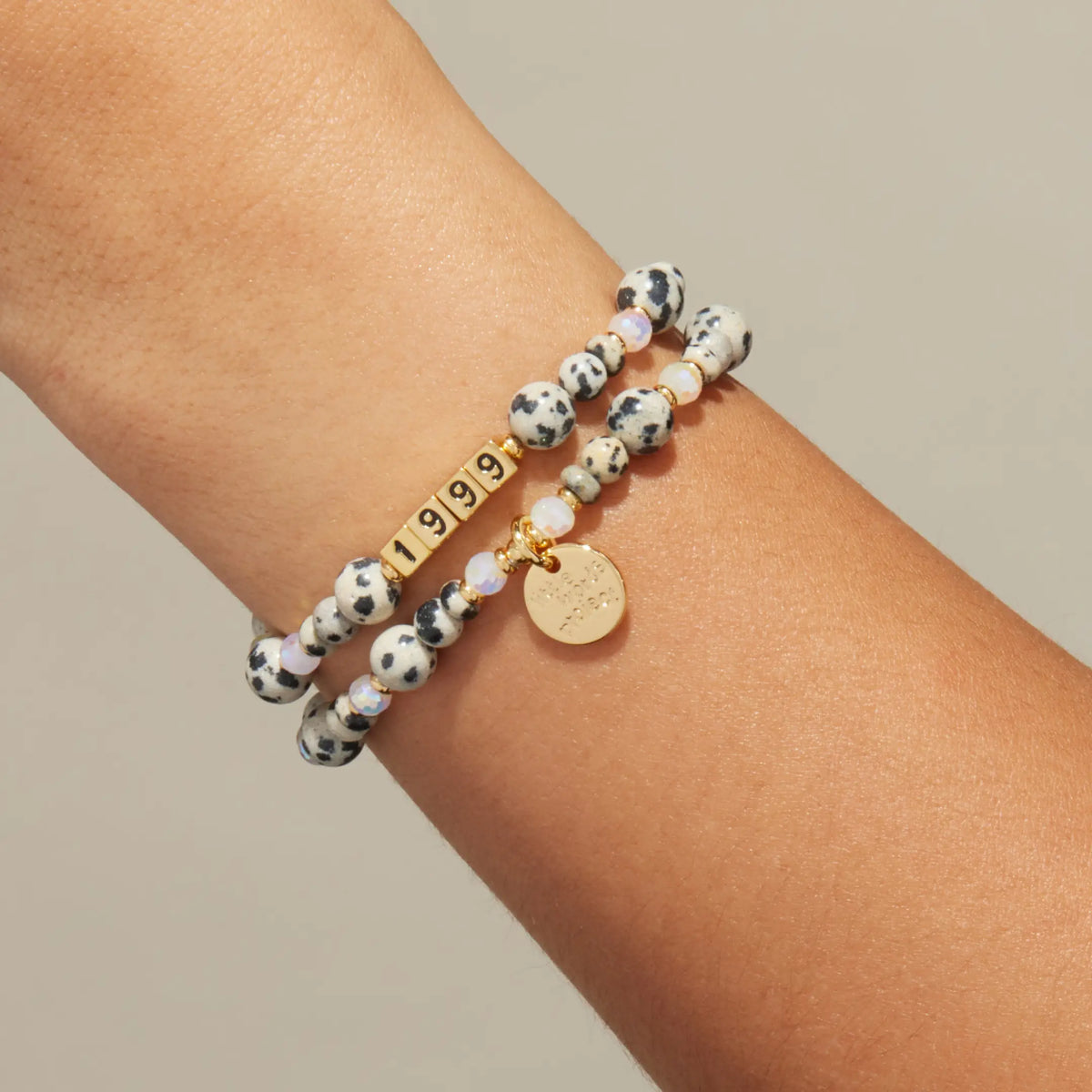Custom Dot Vibes bracelet worn on a wrist, gold letter beads spelling 1999 with dalmatian jasper stone beads